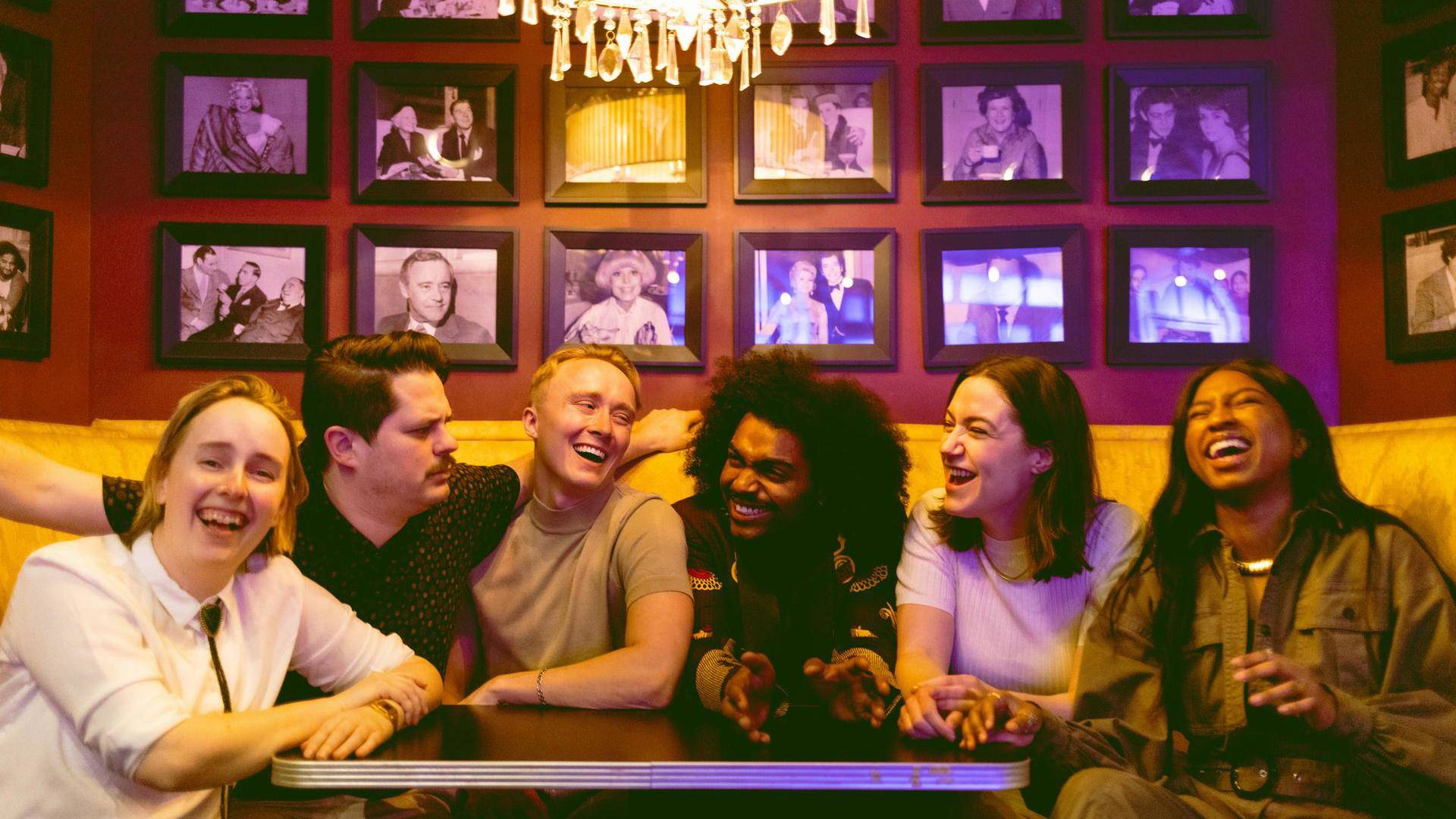 A group of diverse young people sitting close together in a restaurant booth smiling and laughing.