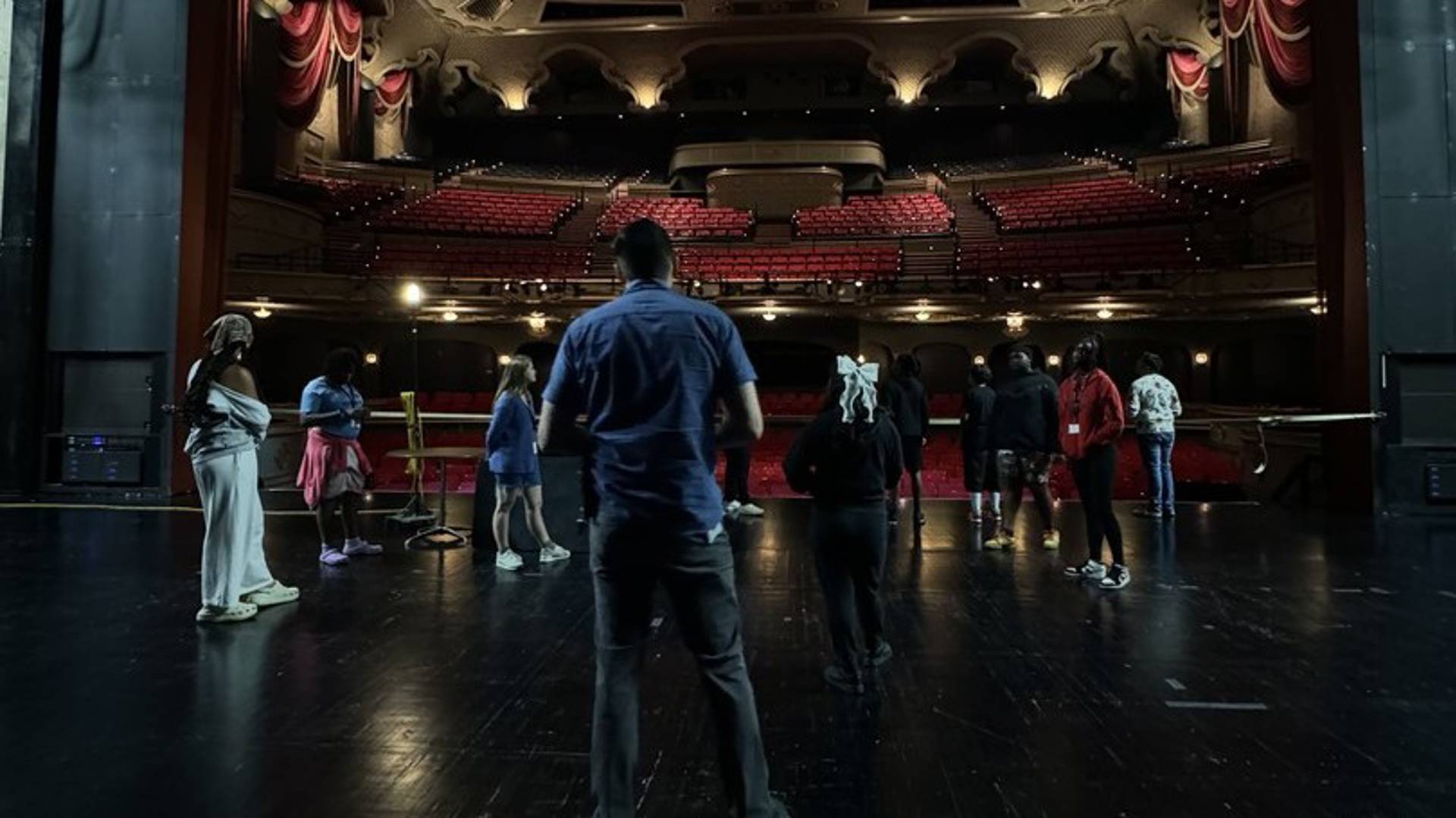 Students in Capitol Theater on stage with the red hall seating in the backgorund.