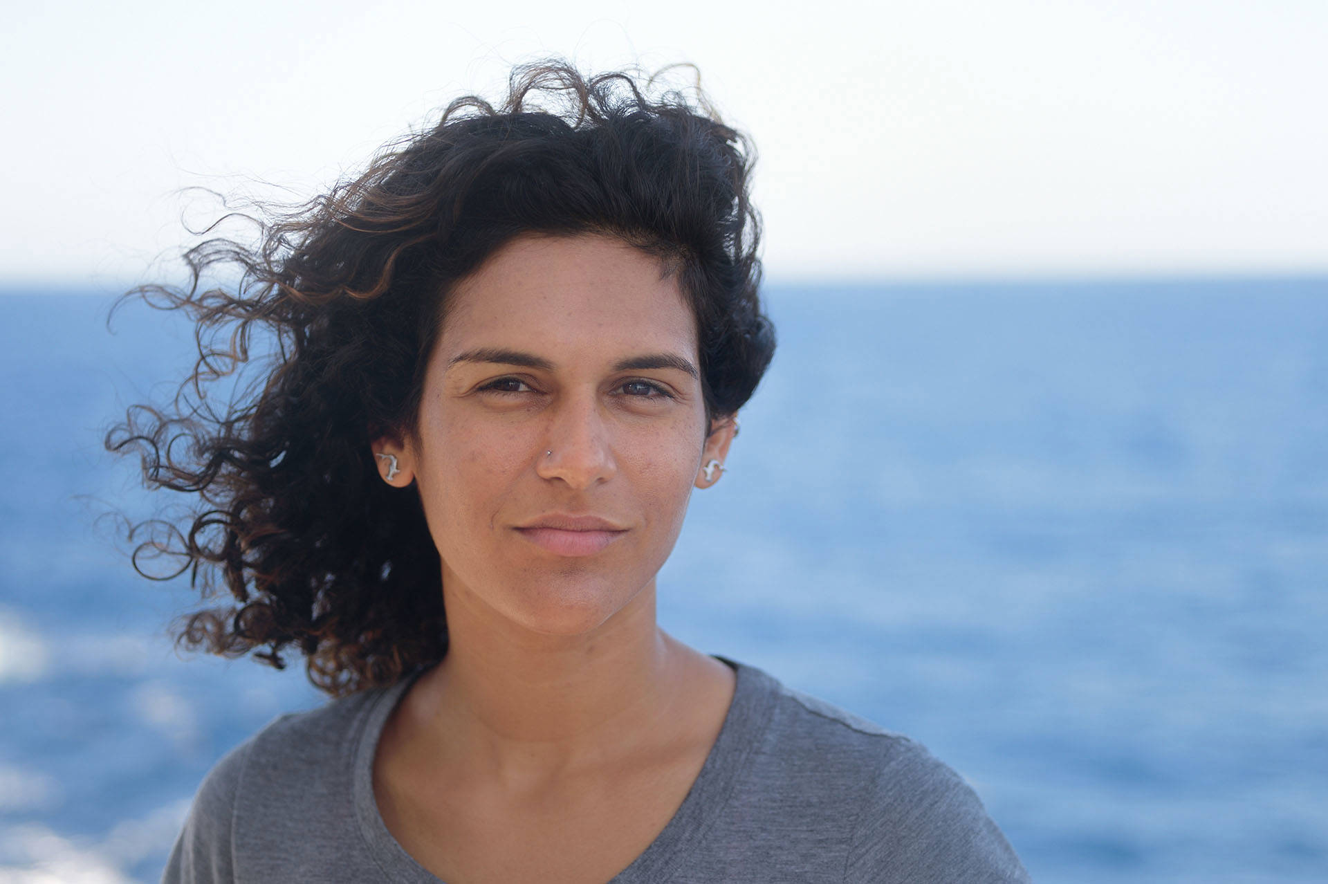 Headshot of Diva Amon. She has dark wavy hair, brown eyes, and a grey Tshirt on. 