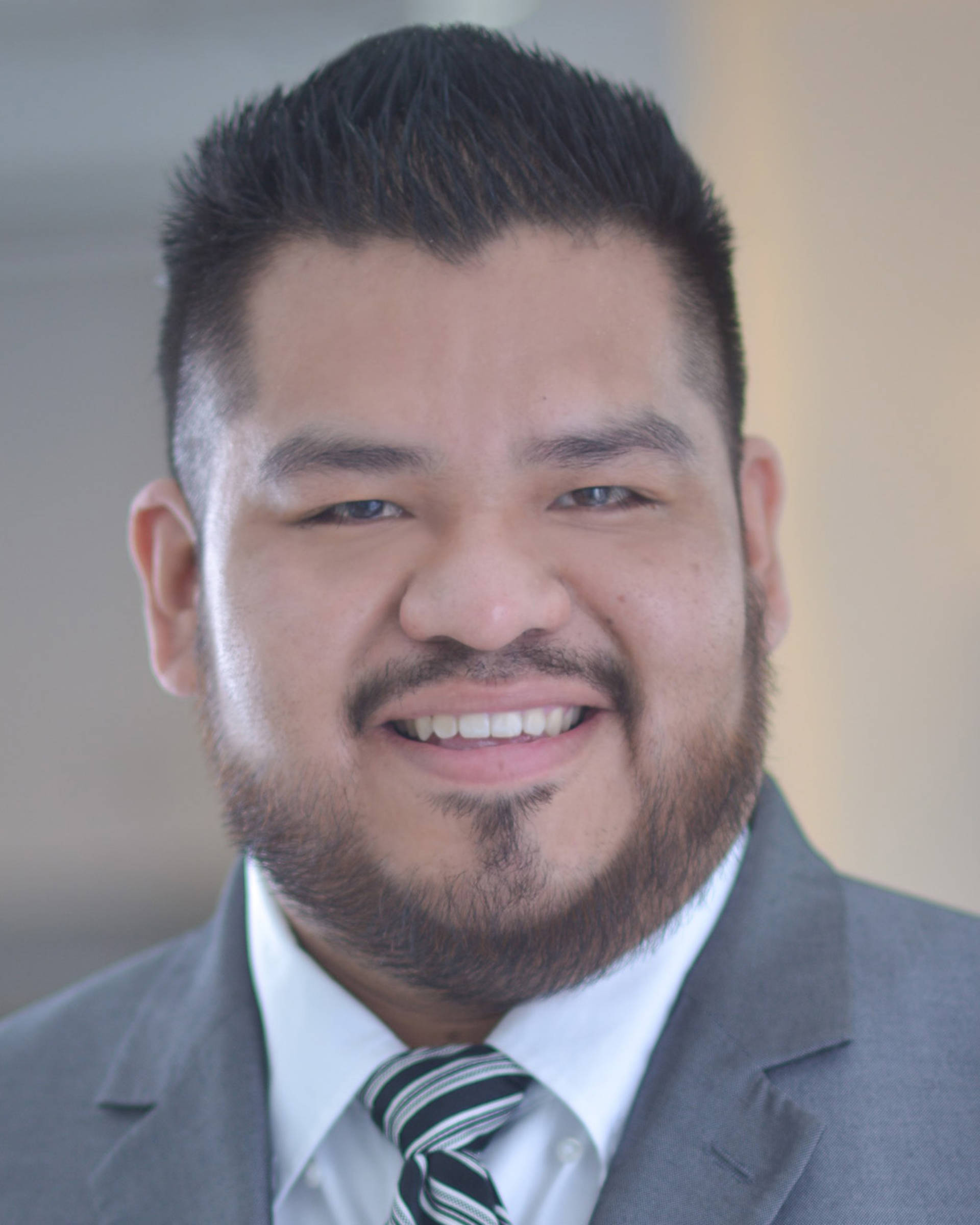 Headshot of a man with medium complexion, short gelled dark hair, brown eyes and a beard in a suit.