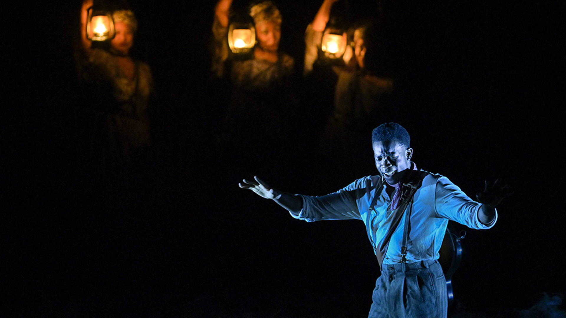 An African American man stands on stage with arms upraised with emotion.