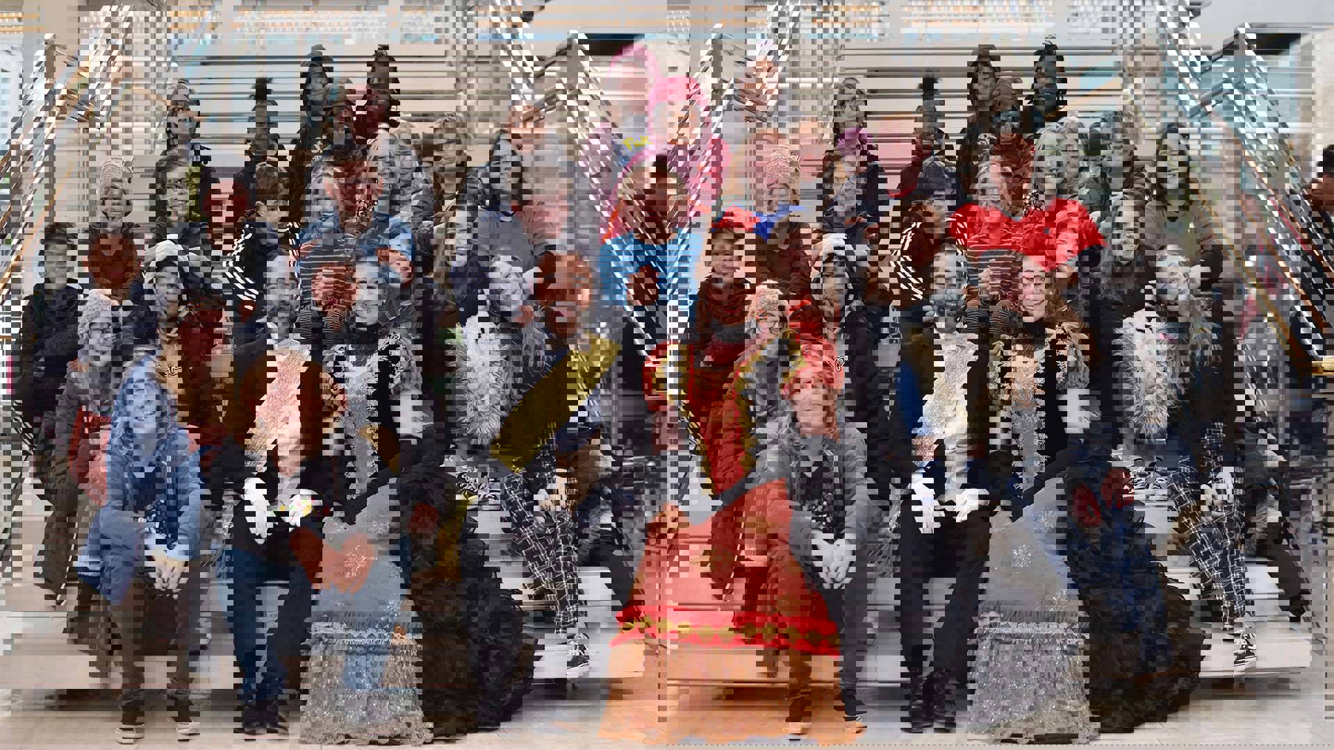 A man and woman in La Traviata opera costumes sitting on steps in front of a group of middle school students.
