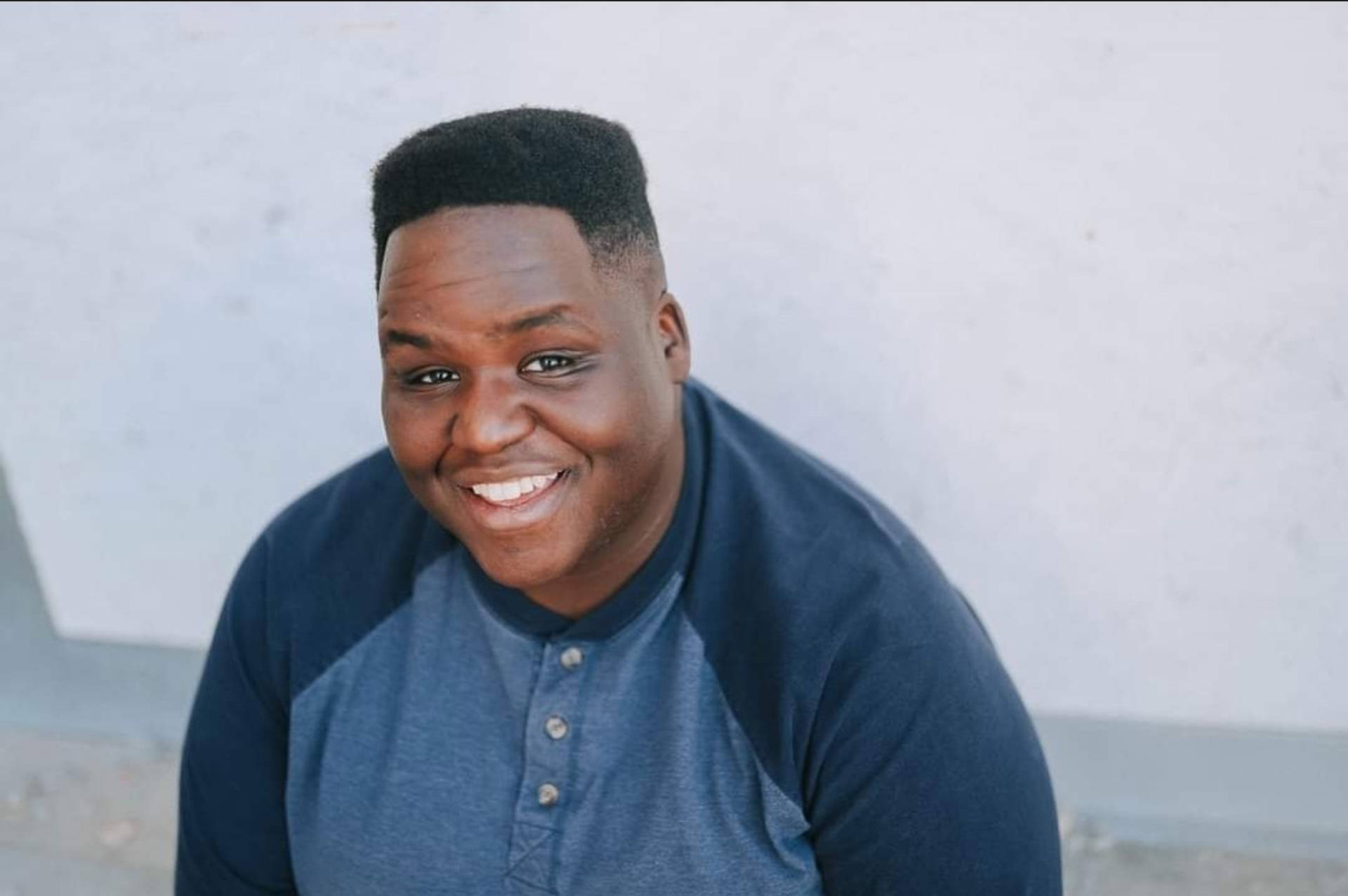 Headshot of asmiling African American man with short hair in a blue shirt with three buttons.