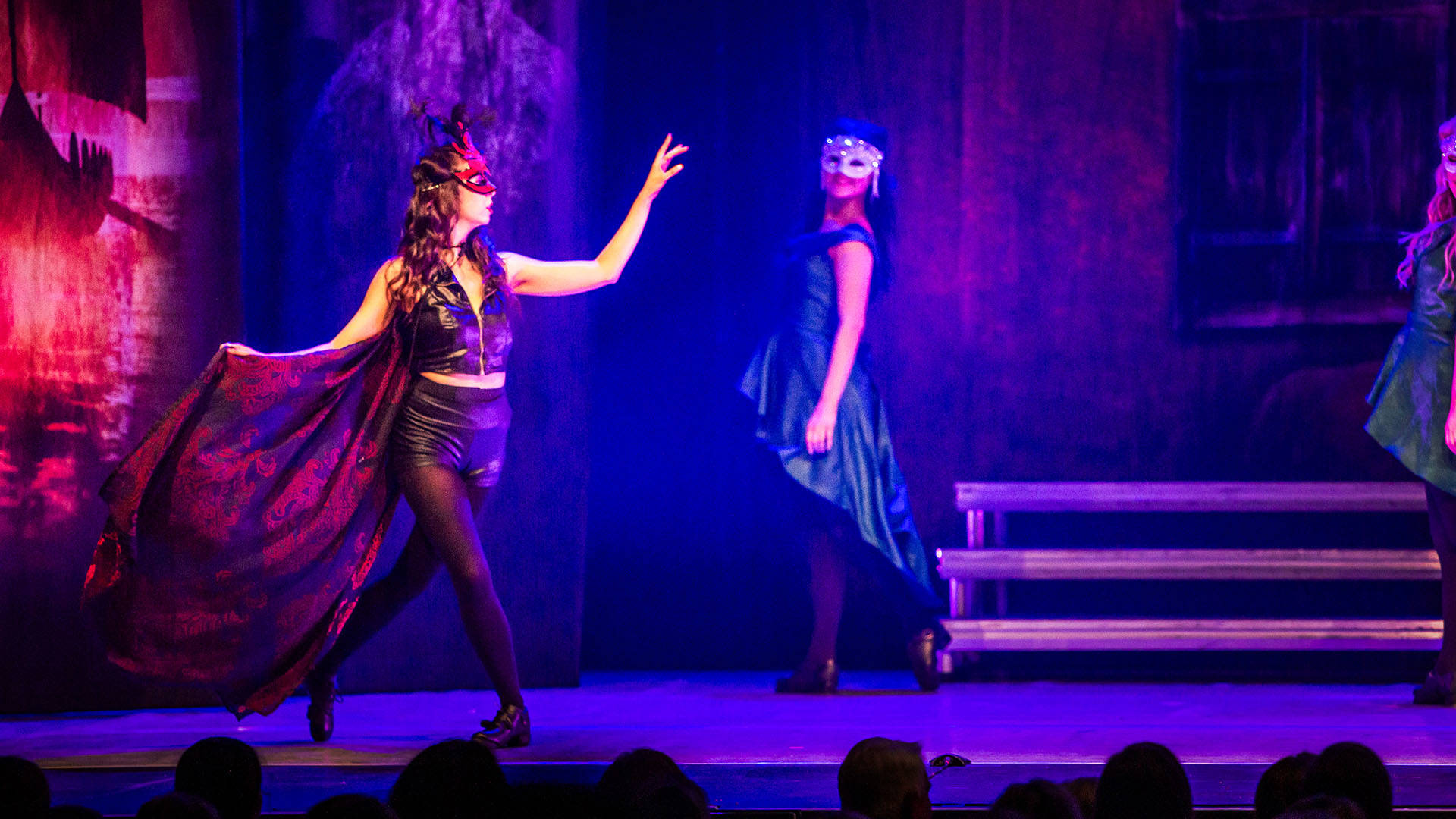 Two women in ornate masks and dresses performing on stage.