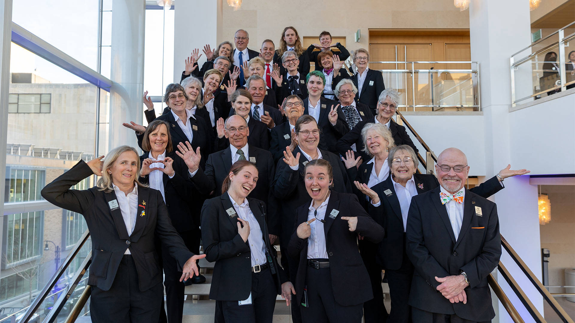 A group of Overture volunteers in dark jackets and white shirts posing for a silly photo on a stair set.