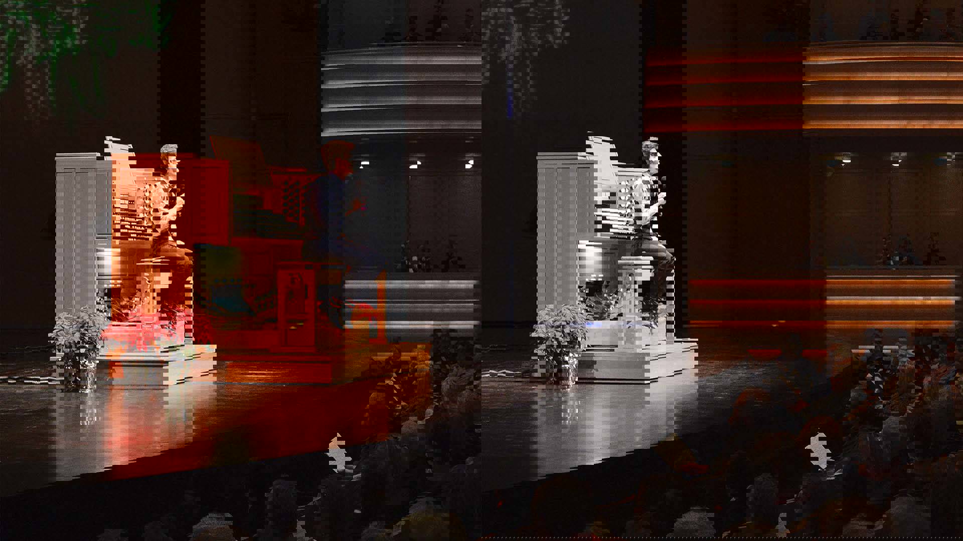 A younger, white man sitting at an organ console on stage decorated with poinsettias. 