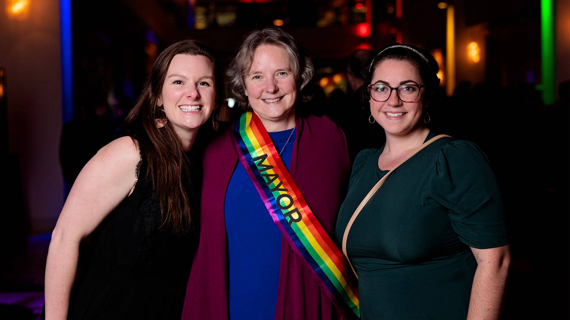Mayor Satya Rhodes-Conway with a rainbow "mayor" sash poses with two other women for a photo.
