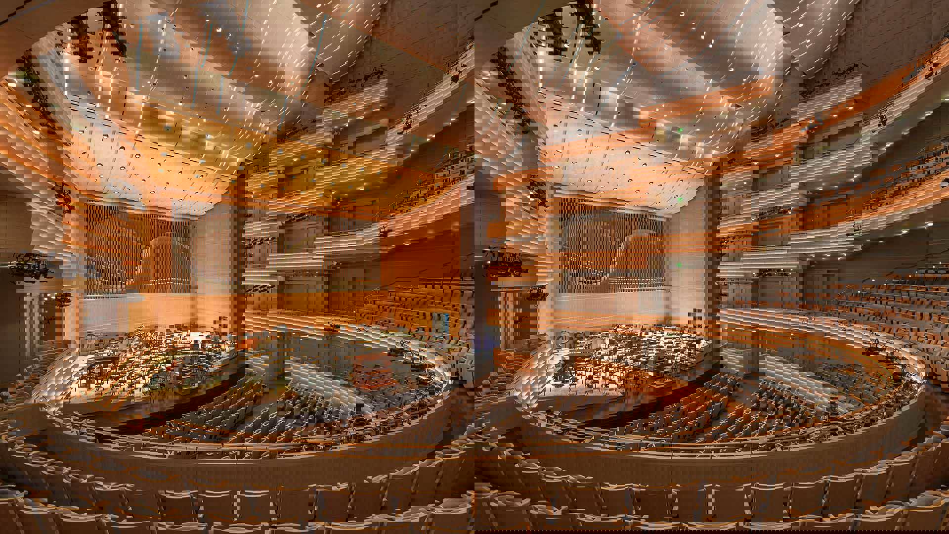 Overture Hall empty. A view from the second level looking on a stage filled with chairs and music stands. Behind the stage are organ pipes.