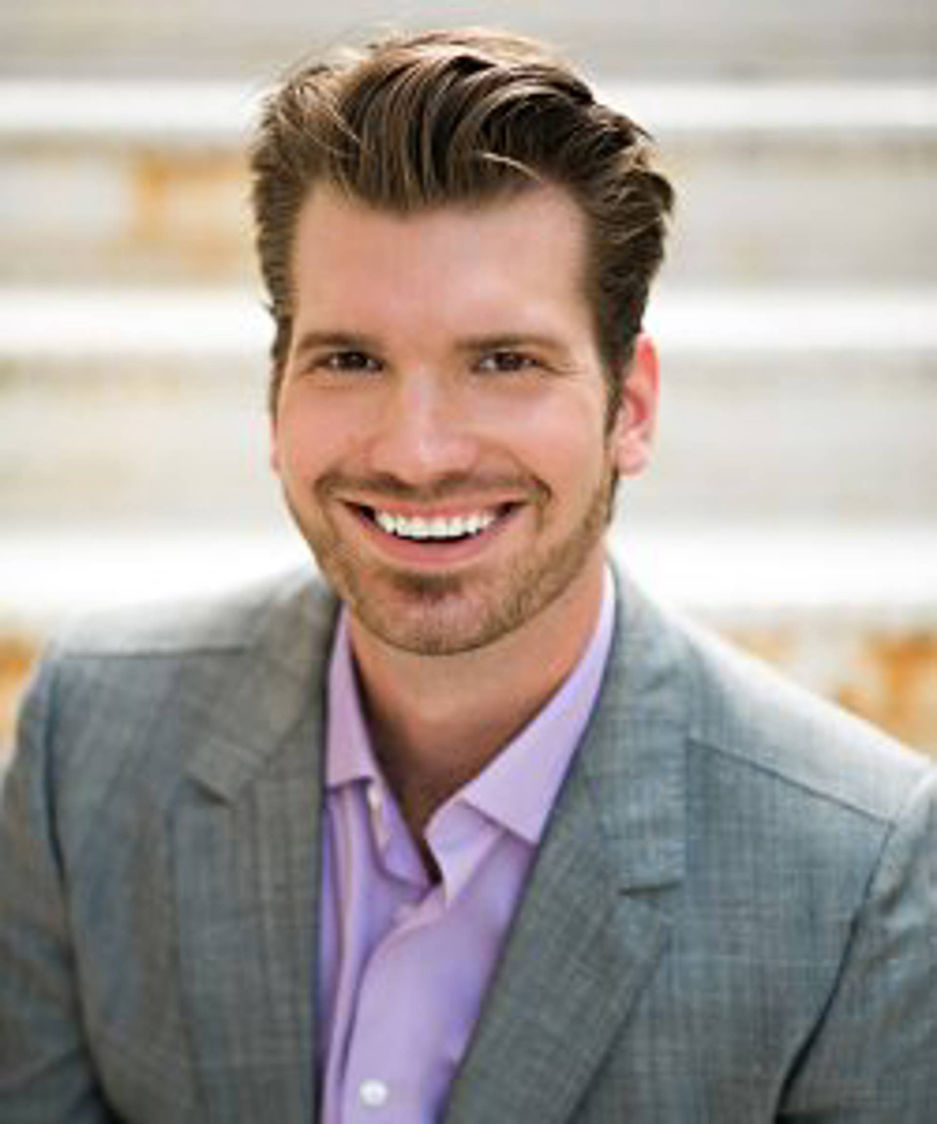 Headshot of a caucasian man with dark eyes and short brown hair in a grey suit.