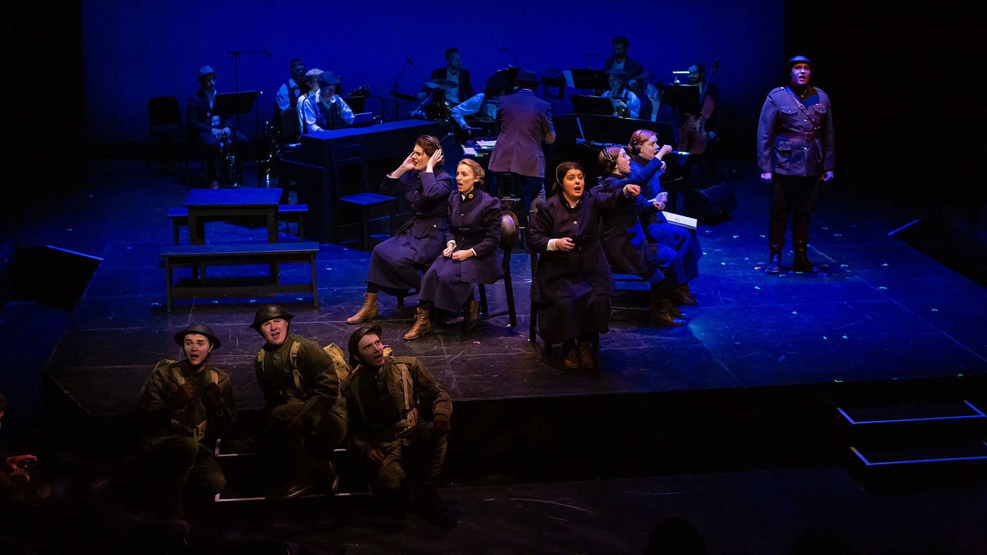 Stage with multiple cast members wearing military uniforms and singing during a performance of "The Hello Girls."