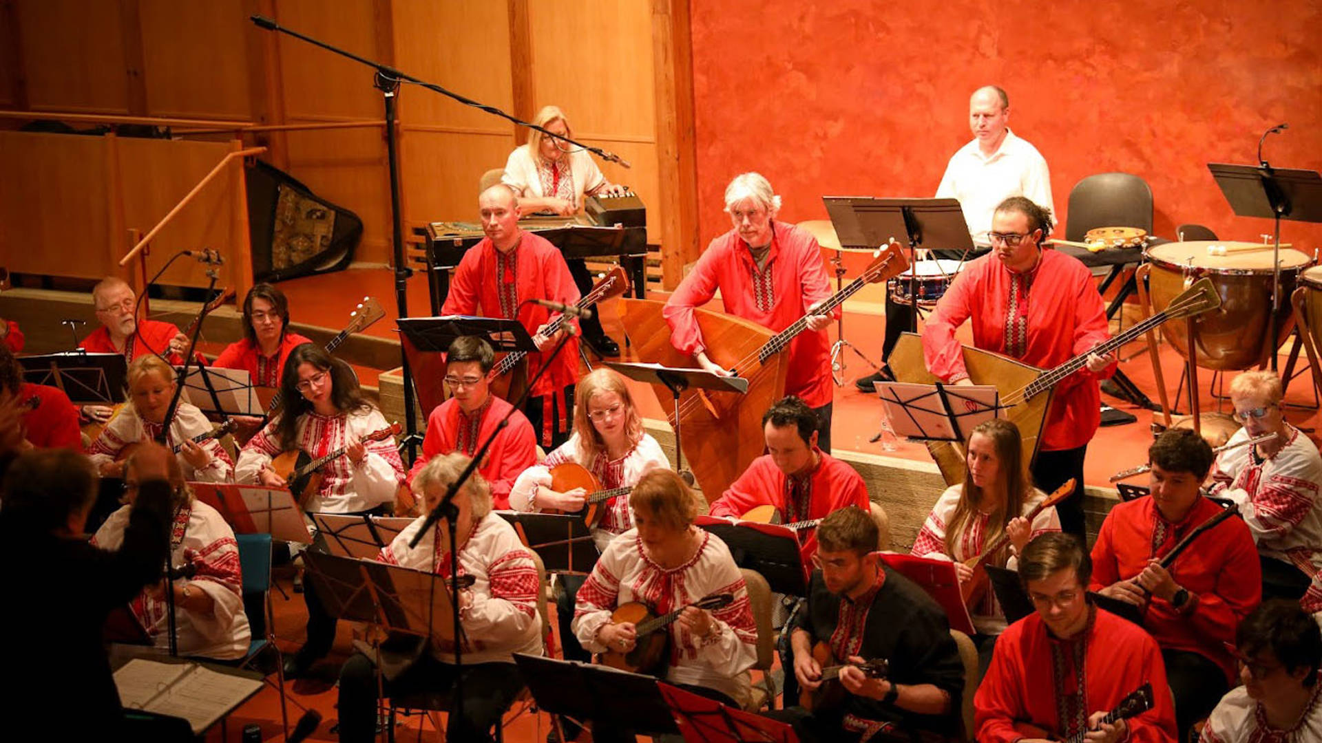 A russian folk orchestra rehearsing on a stage. Several members are standing and playing large string instruments.