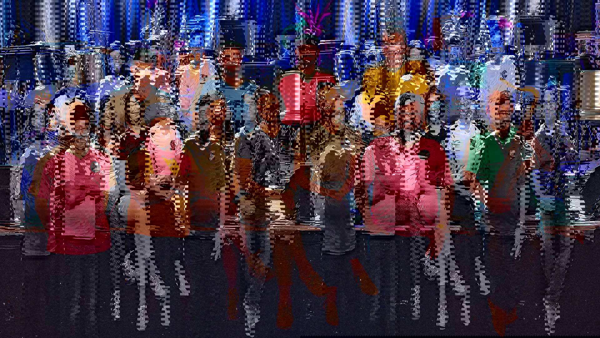 A group of adults in colorful jerseys standing in front of a stage. One man is holding a saxophone.