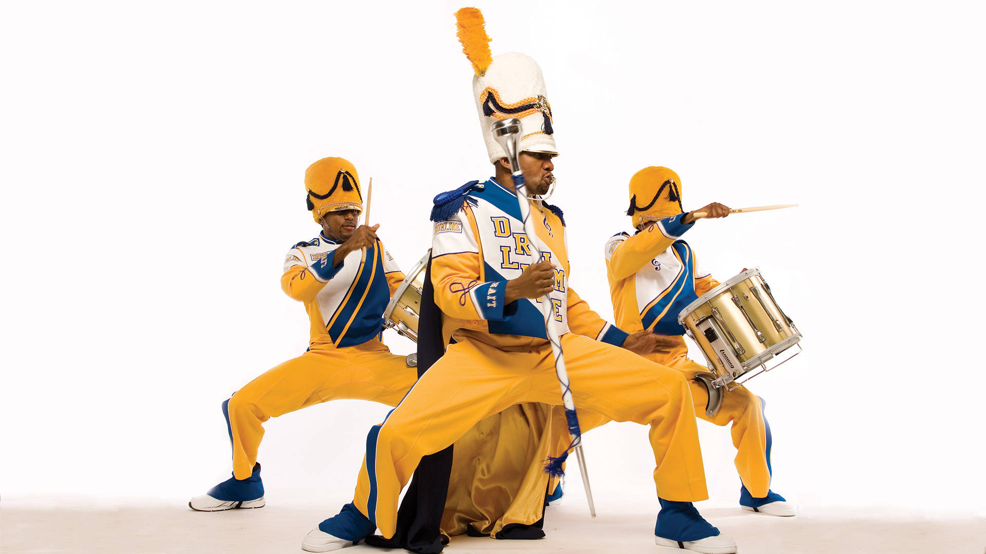 A drum major and two marching snare drummers in yellow and blue uniforms performing against a beige background