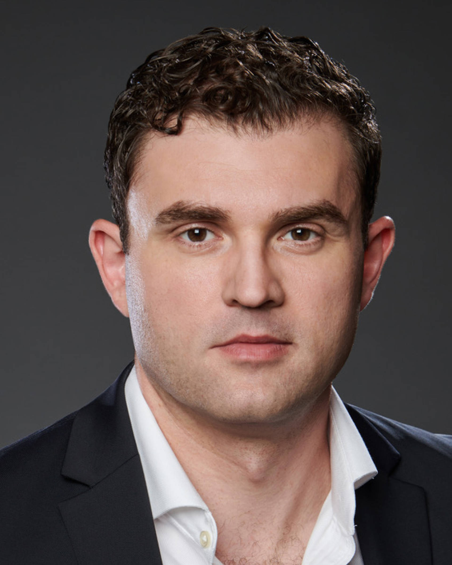 Headshot of a caucasian man with short brown hair, brown eyes, and a jacket  with open dress shirt.