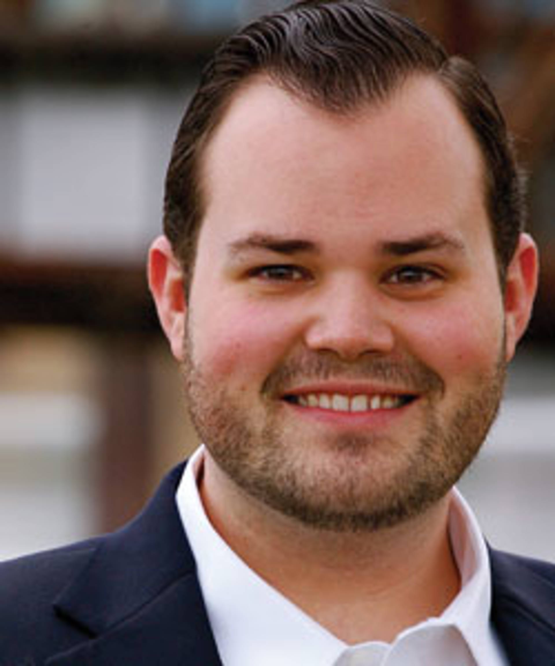Headshot of a smiling caucasian man with brown eyes, short beard and combed brown hair