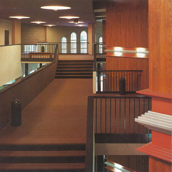 A lobby in the 1990s with multiple levels, brown carpeting, wood panel walls and raillings