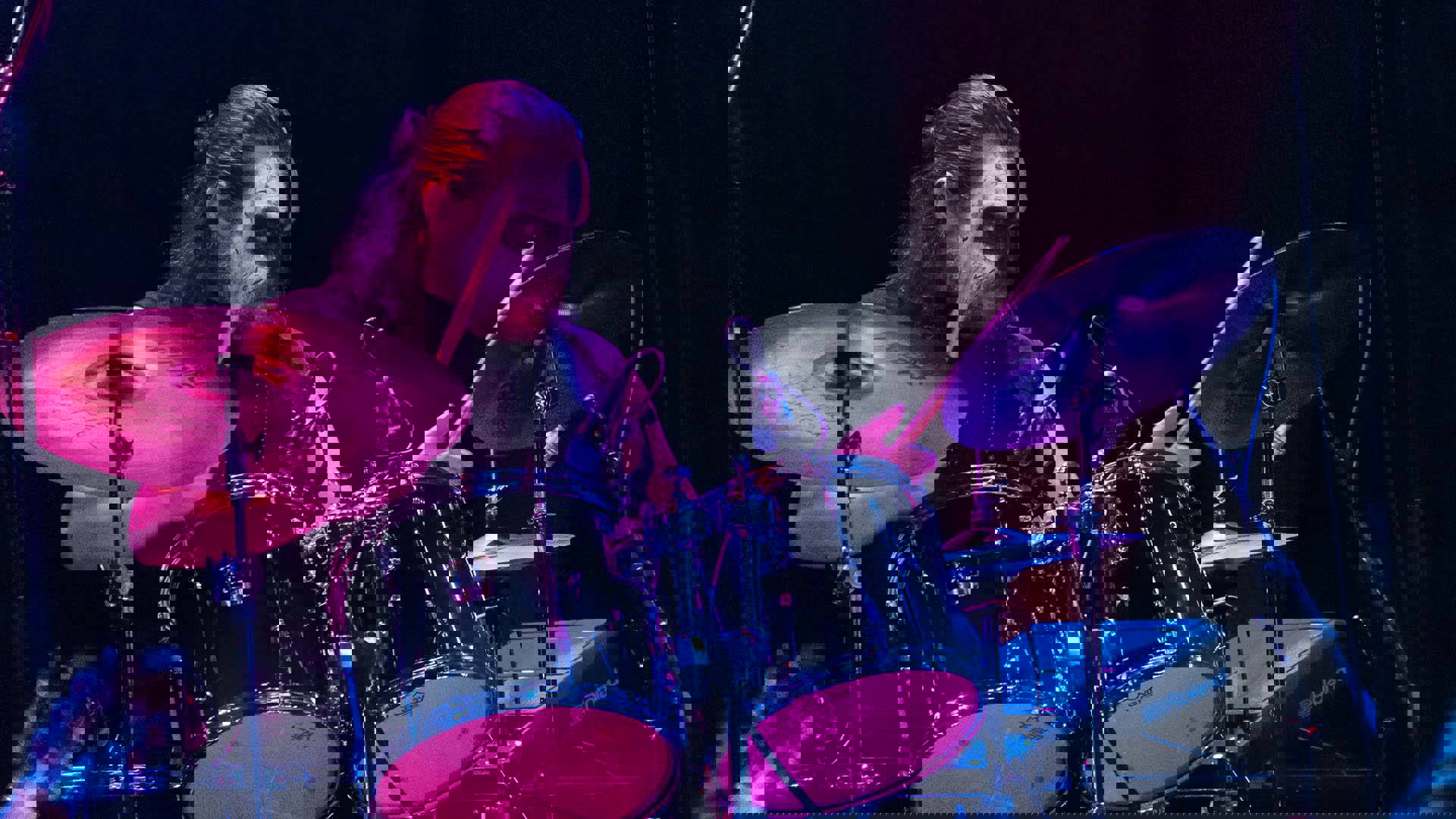 A man with long hair and black and white face paint plays a drumset.