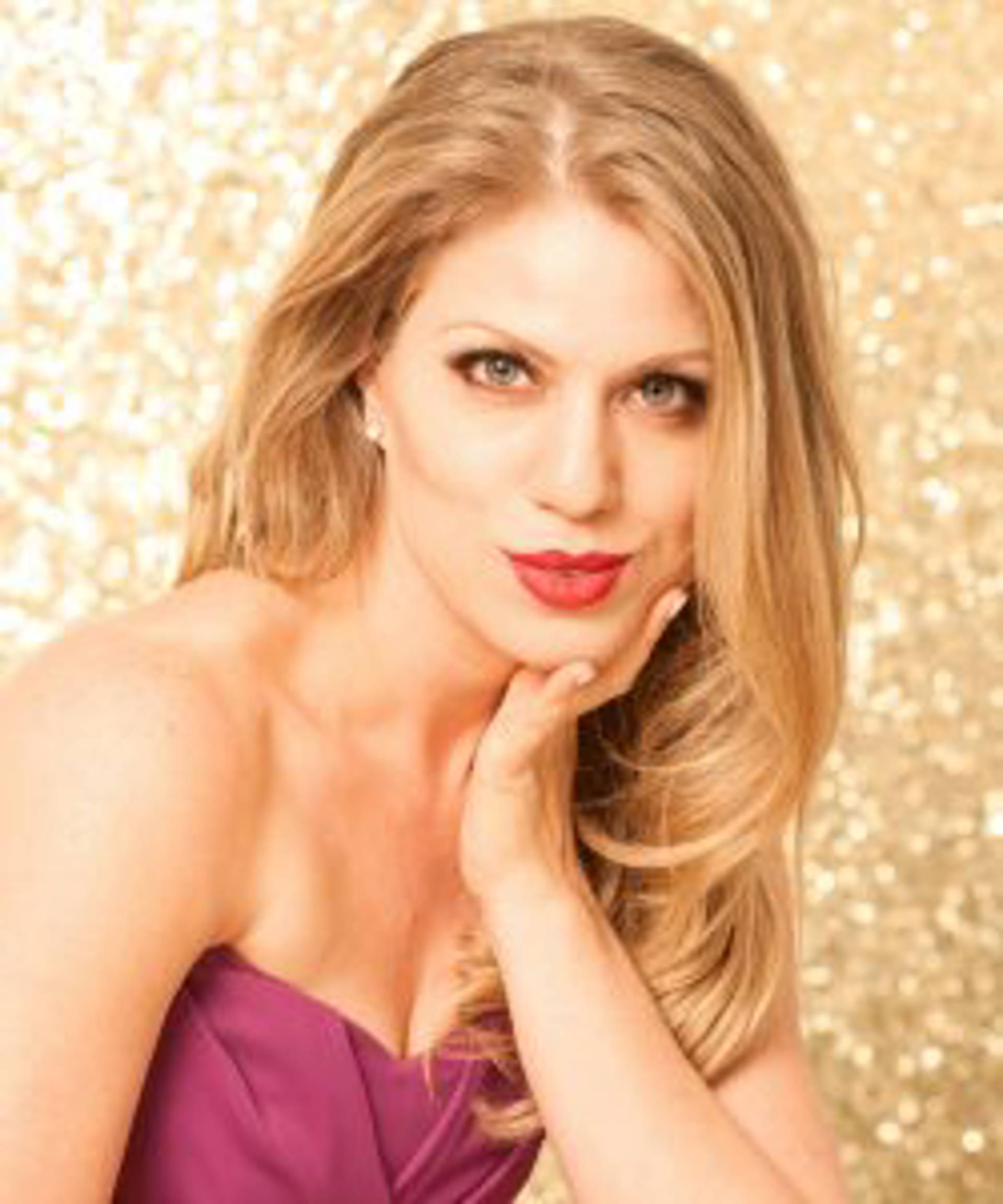 Headshot of a caucasian woman with blond hair and blue eyes in a purple dress.
