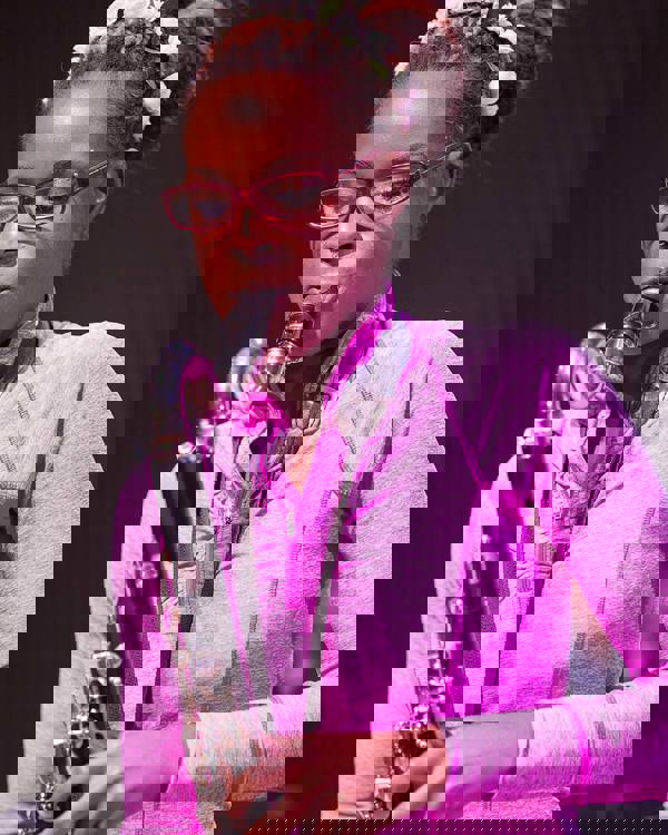 A young woman in a pink top playing a bass clarinet.