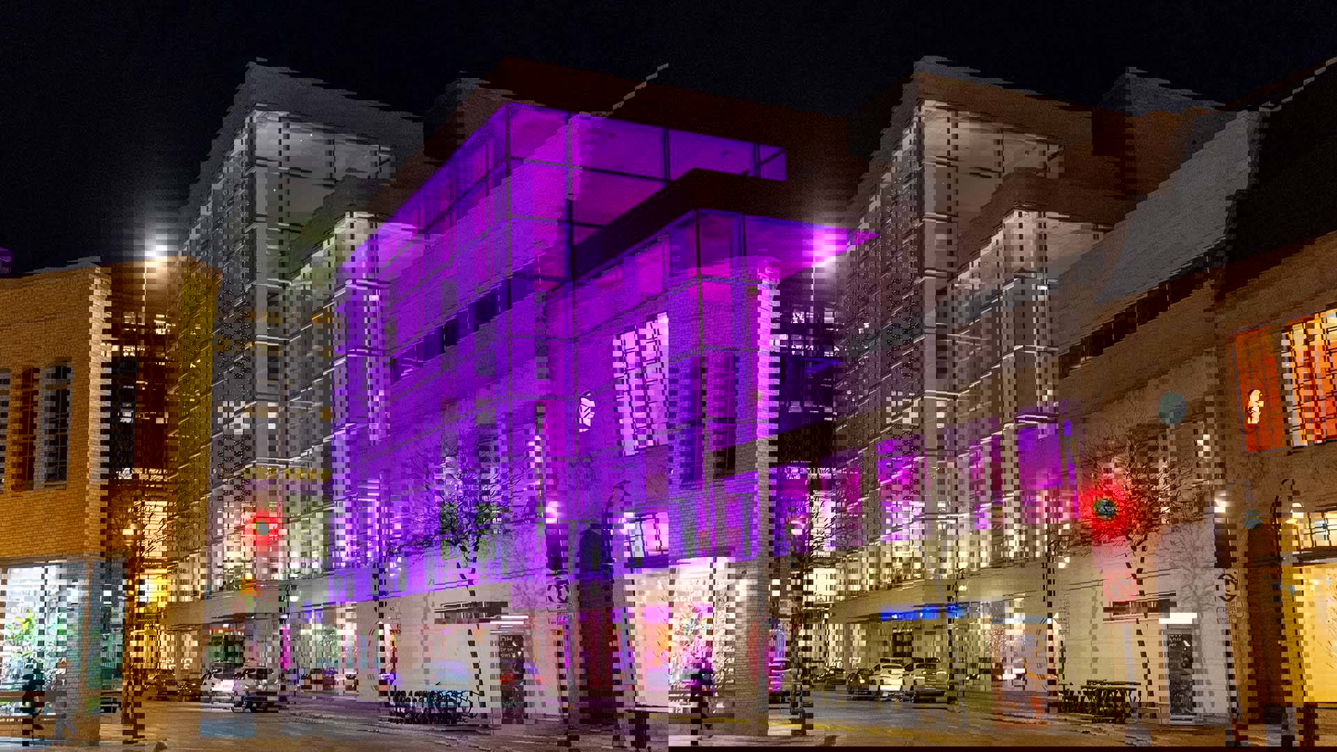 The outside of Overture at nighttime. Purple and pink lights illuminate the inside of Overture Hall through large, glass windows.