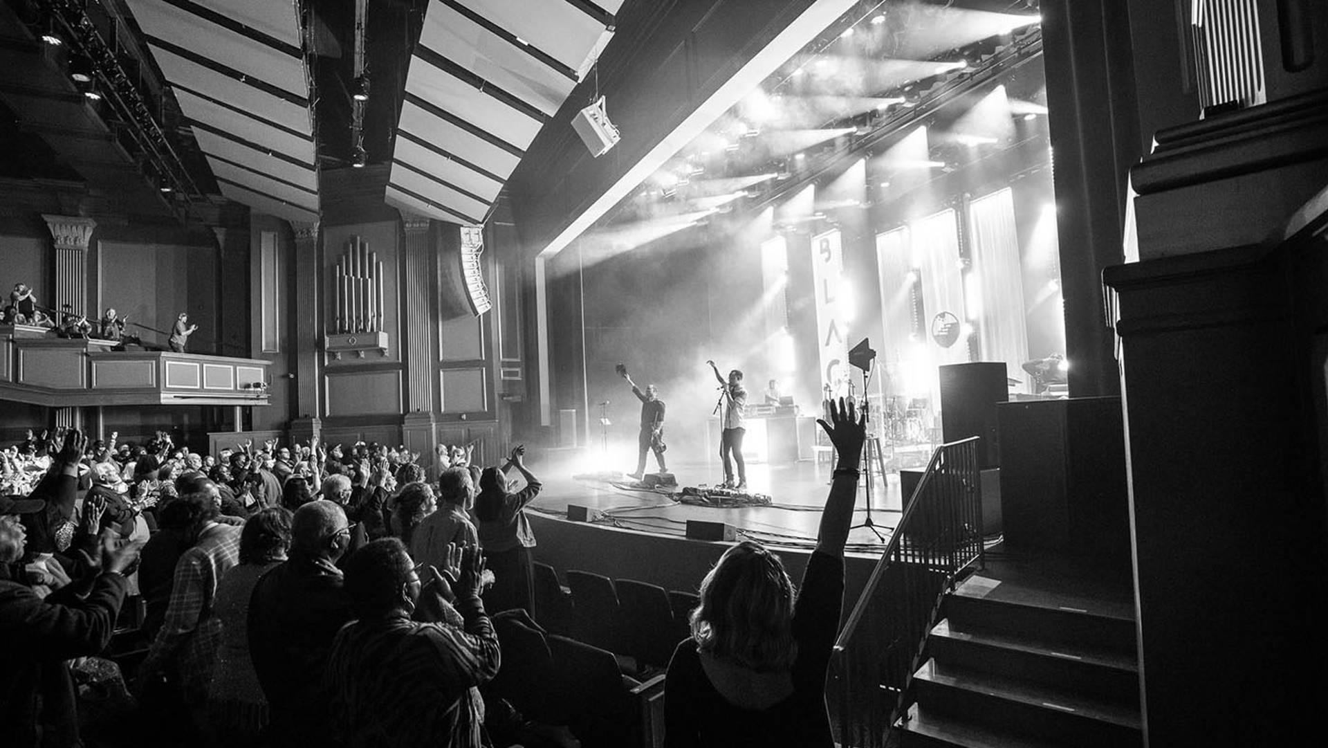 Black Violin performing on stage. The audience is standing up and clapping.