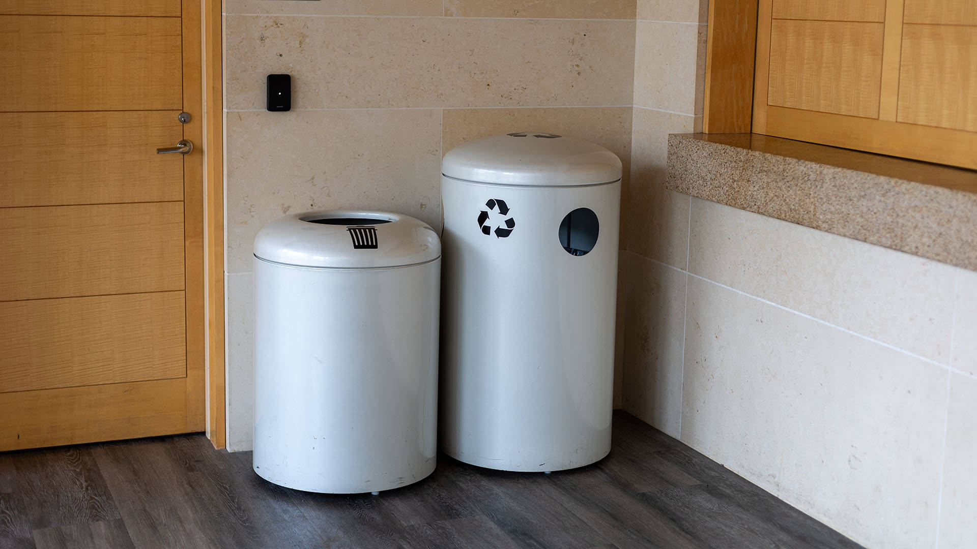 Two large white metal trash receptacles in Overture Hall Lobby, one with a black trash-bin sticker, the other with a black recycling arrows sticker.