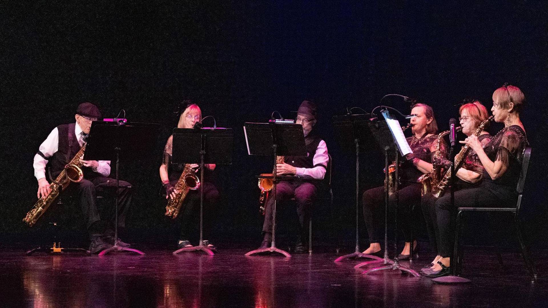 A saxophone sextet performing on a dark stage.
