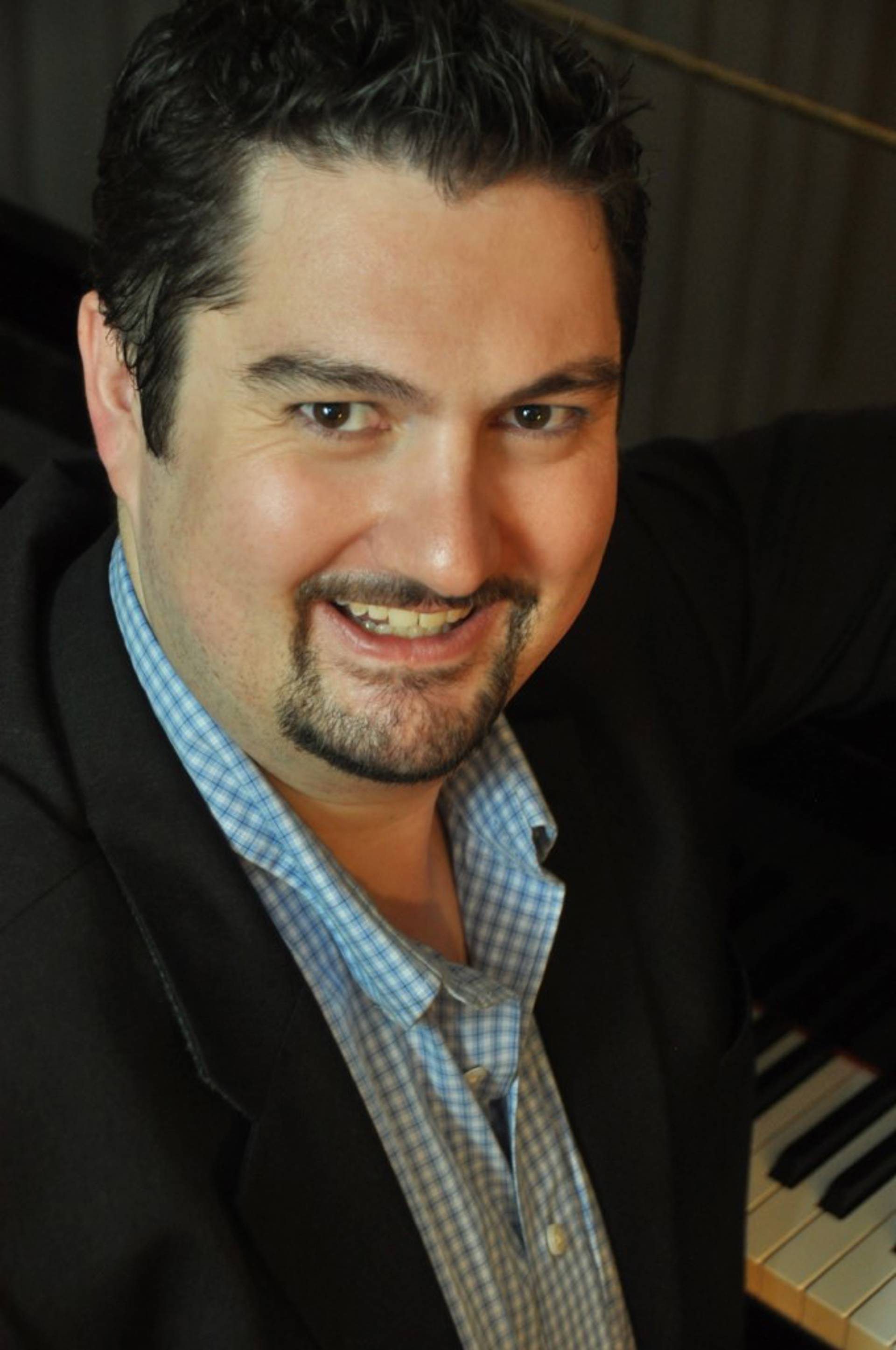 Headshot of a man with light complexion, dark hair, a beard and a suit jacket over dress shirt.