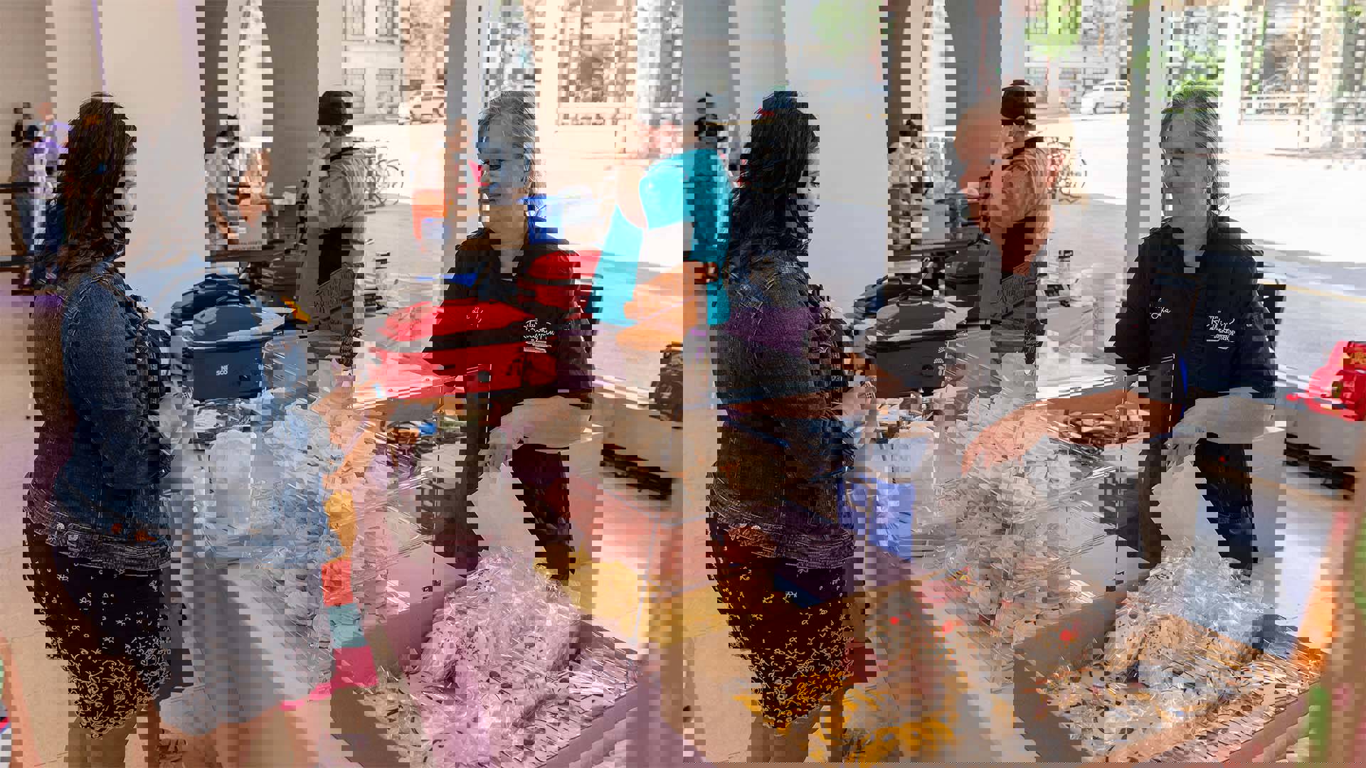 A woman selling colorful treats to another woman and her child in a white lobby.