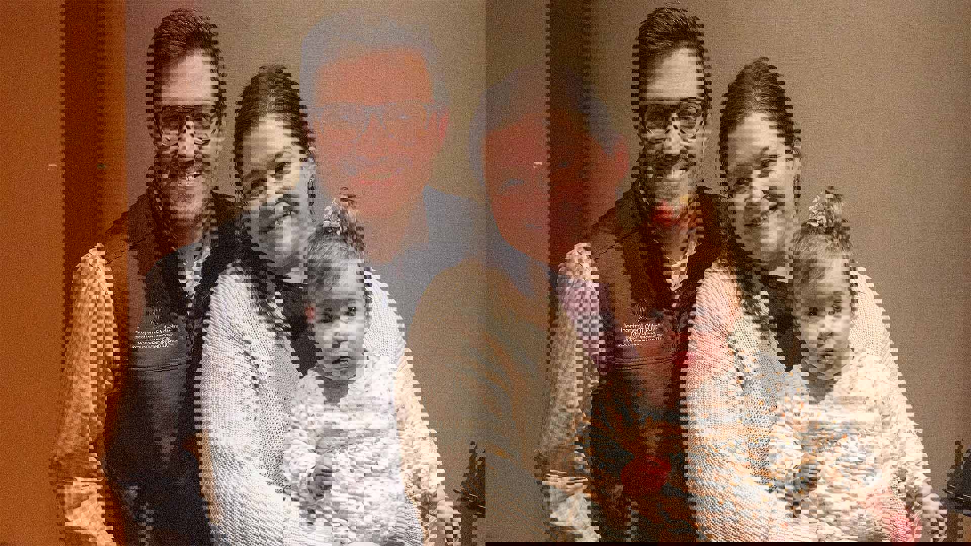 A father, mother and infant child pose and smile for a photo.