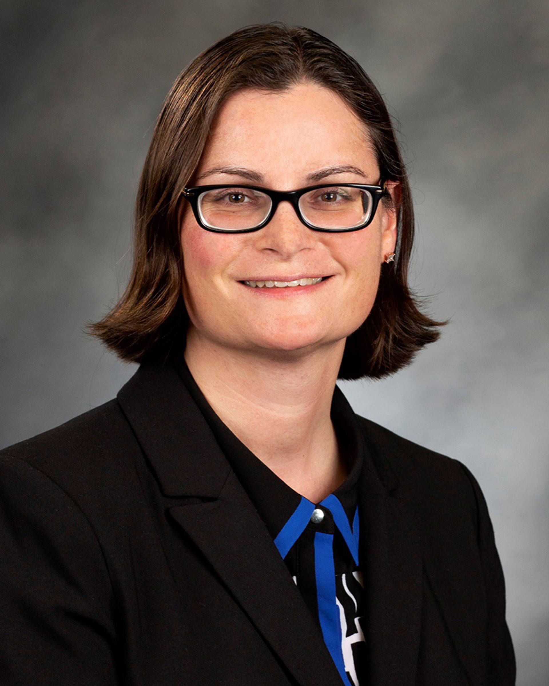Headhot of a woman with light complexion, brown eyes and medium length hair. She has a dark outfit on and glasses