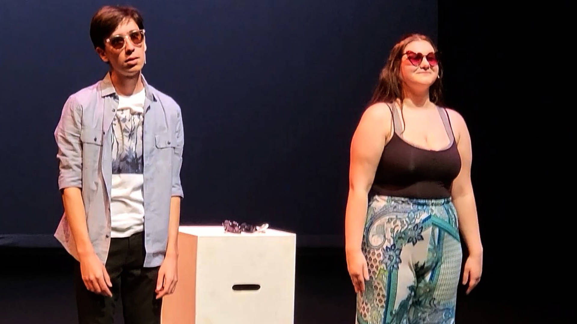 Two high school students performing theater. They are wearing warm weather clothing and sunglasses