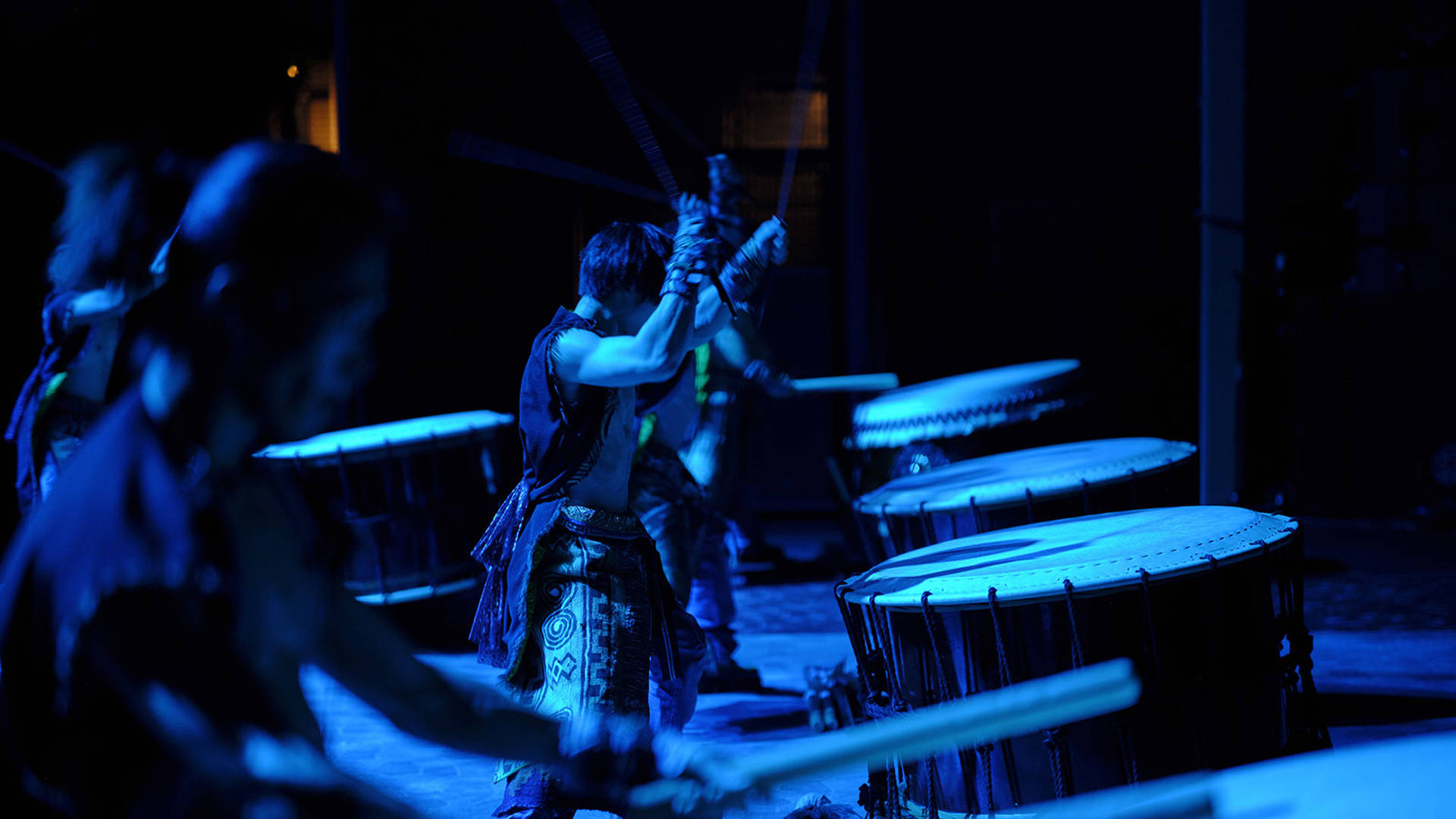 YAMATO drummers in dark blue lighting performing on stage in a row.