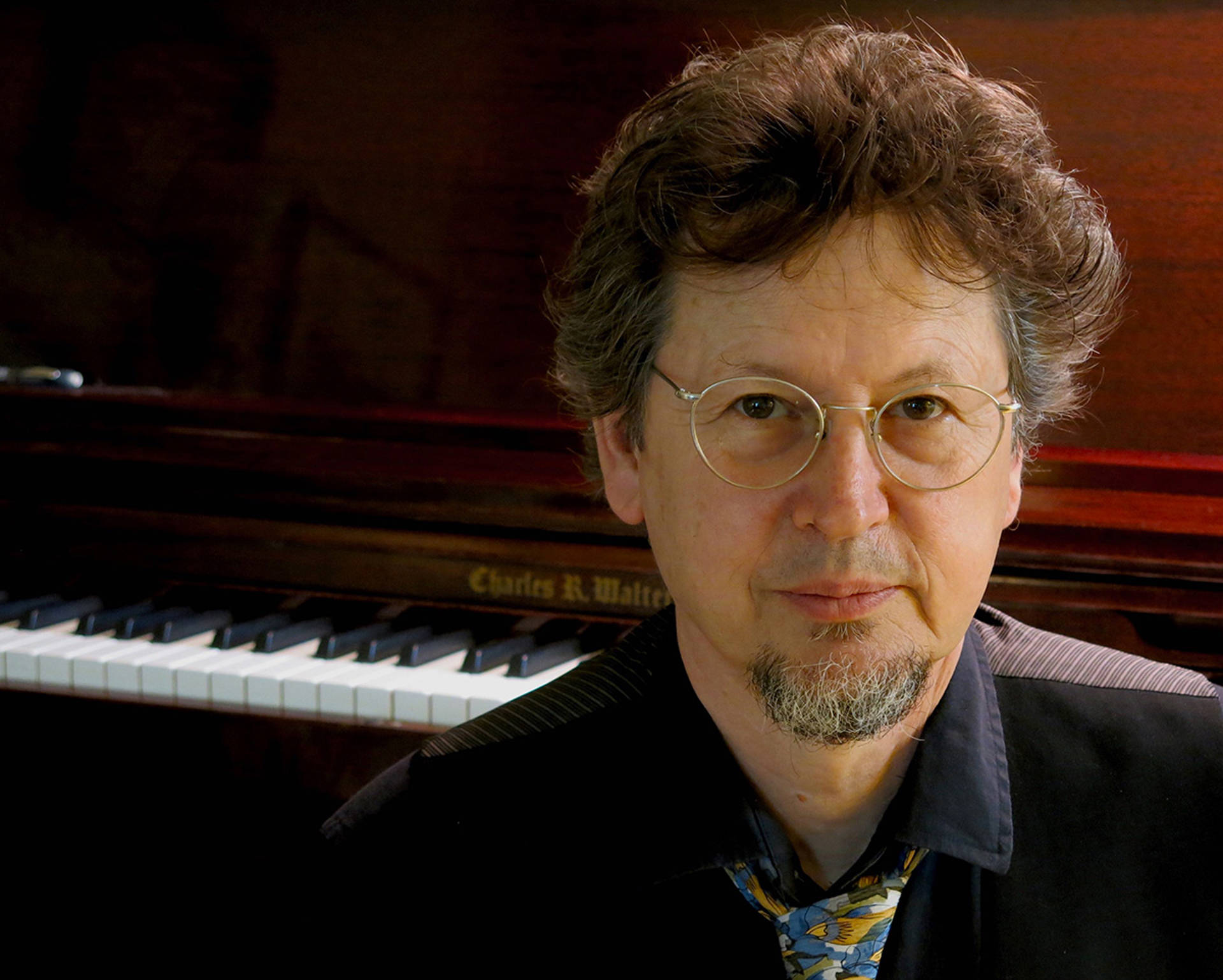Headshot of a middle aged man with brown and grey hair in front of a piano.