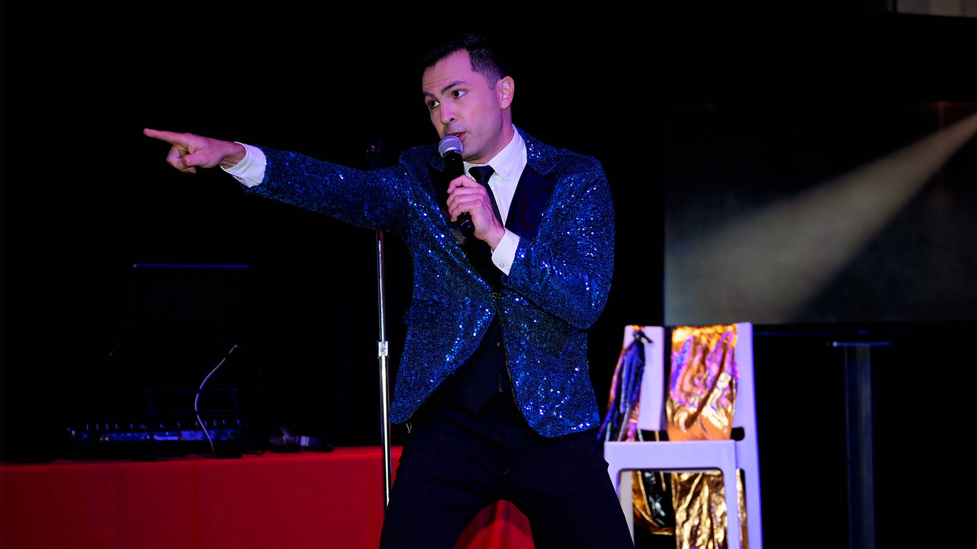 A man in a glittery jacket with a microphone points outward.