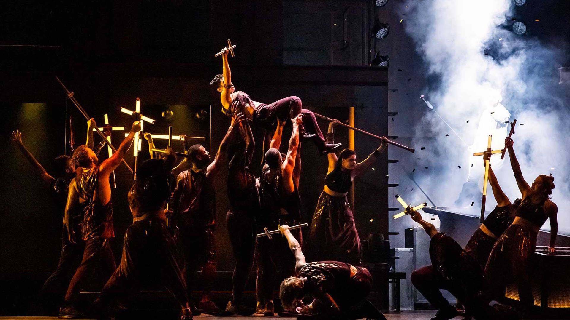 The cast of Jesus Christ Superstar performing on stage. They are holding light up crosses.
