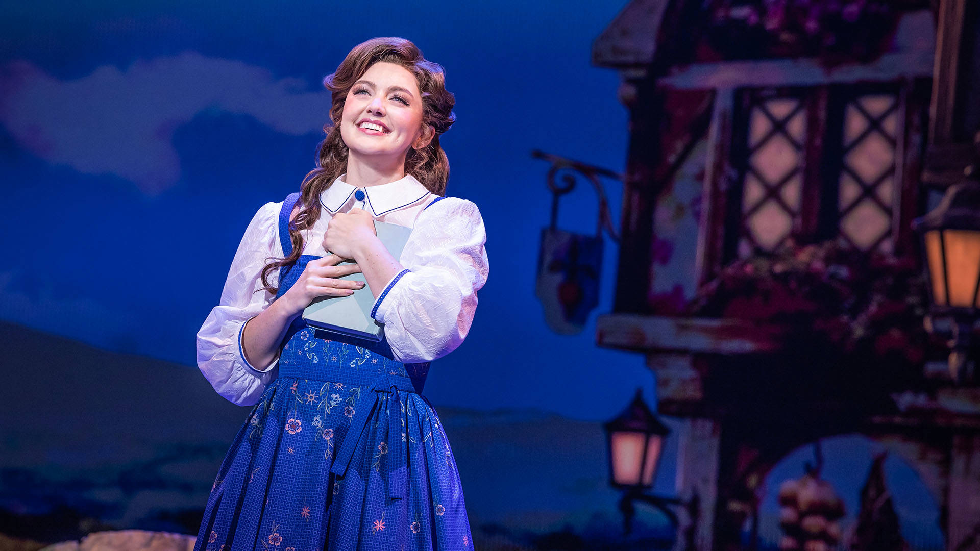 A woman with light complexion and brown hair smiles while holding a light blue book.
