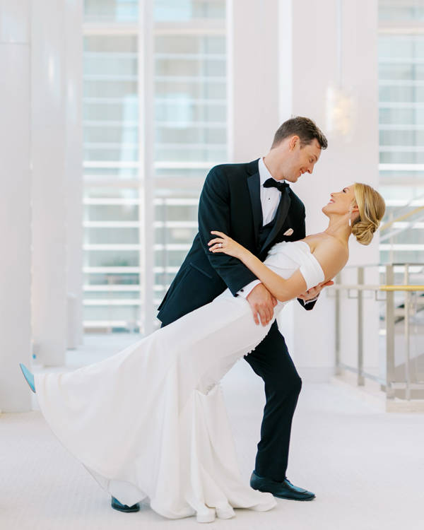A white couple on their wedding day in a black tux and a white gown. the groom is dipping the bride as if they are dancing.