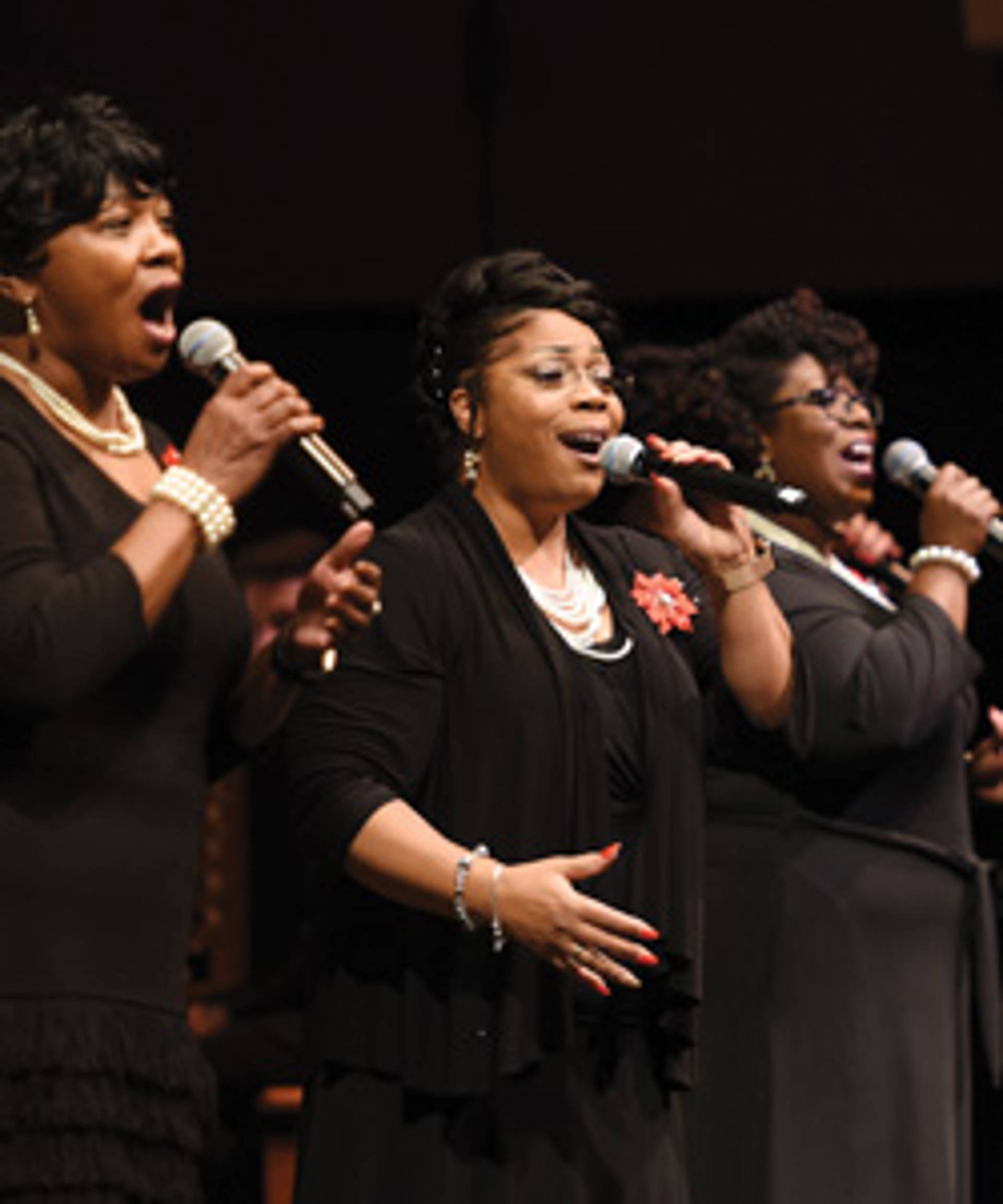 Three african american women singing in dark outfits.