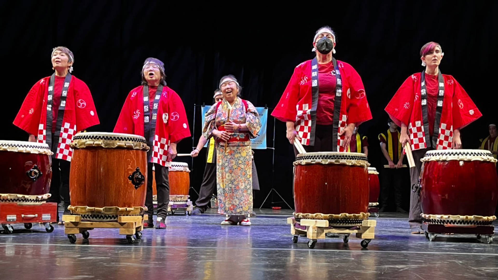Four drummers in red robes performing on stage.