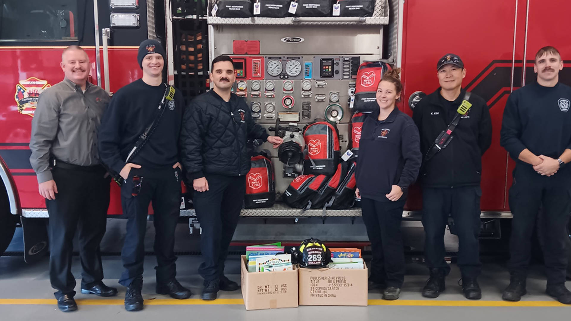 Six firefighters smiling for a photo with two boxes full of books.