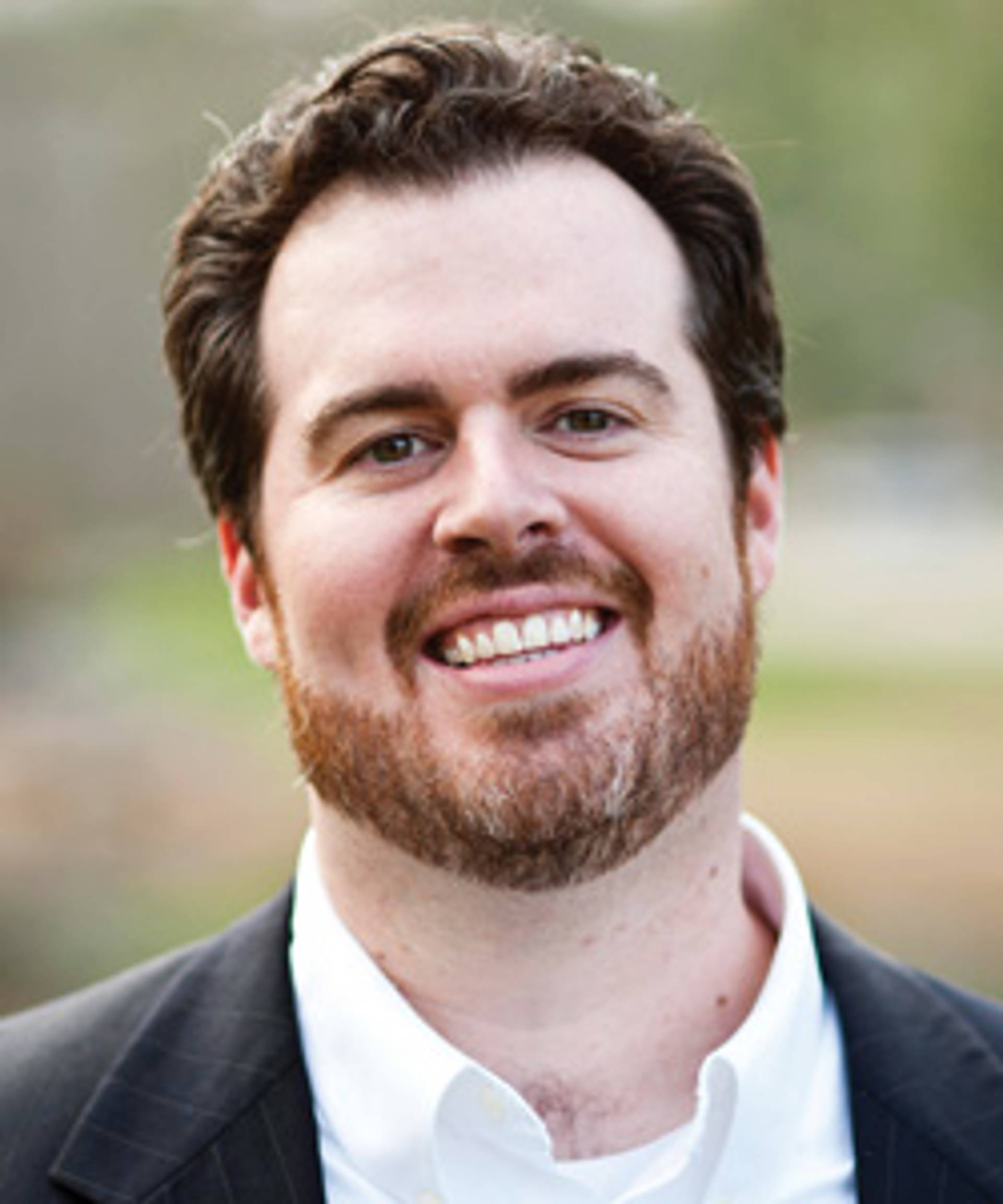 A light skinned man with a short red beard, dark hair and dark eyes.