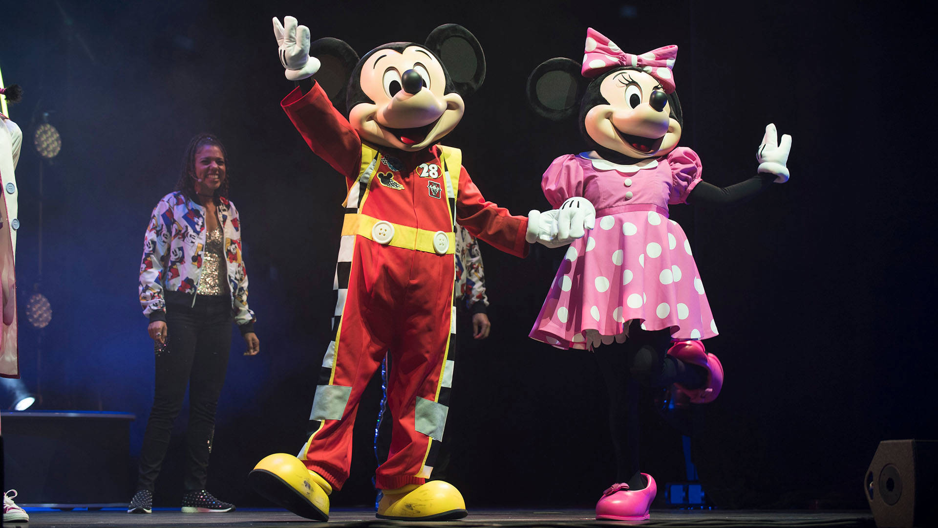 Mickey Mouse and Minnie Mouse costumes holding hands and waving to an audience.