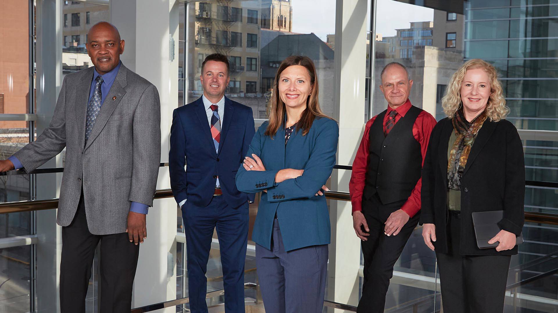 Five members of the leadership team stand in front of a glass wall.