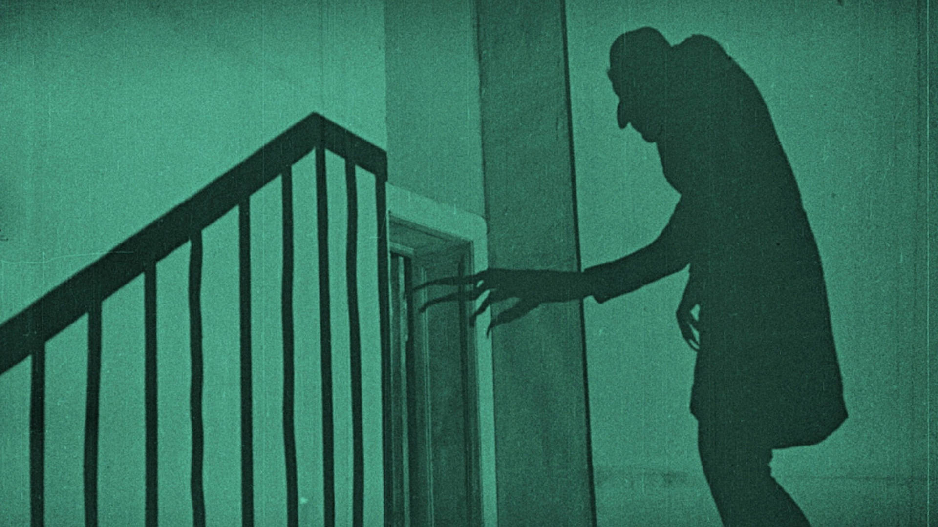A shadow of a scary hunched figure with long fingers and a bald head cast against a green wall. A banister shadow and door frame are also visible.