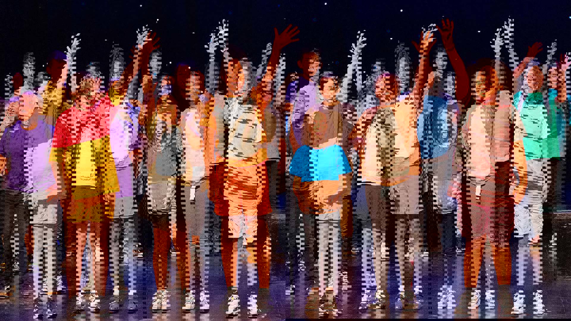 Young students in colorful costumes performing on a dark stage. 
