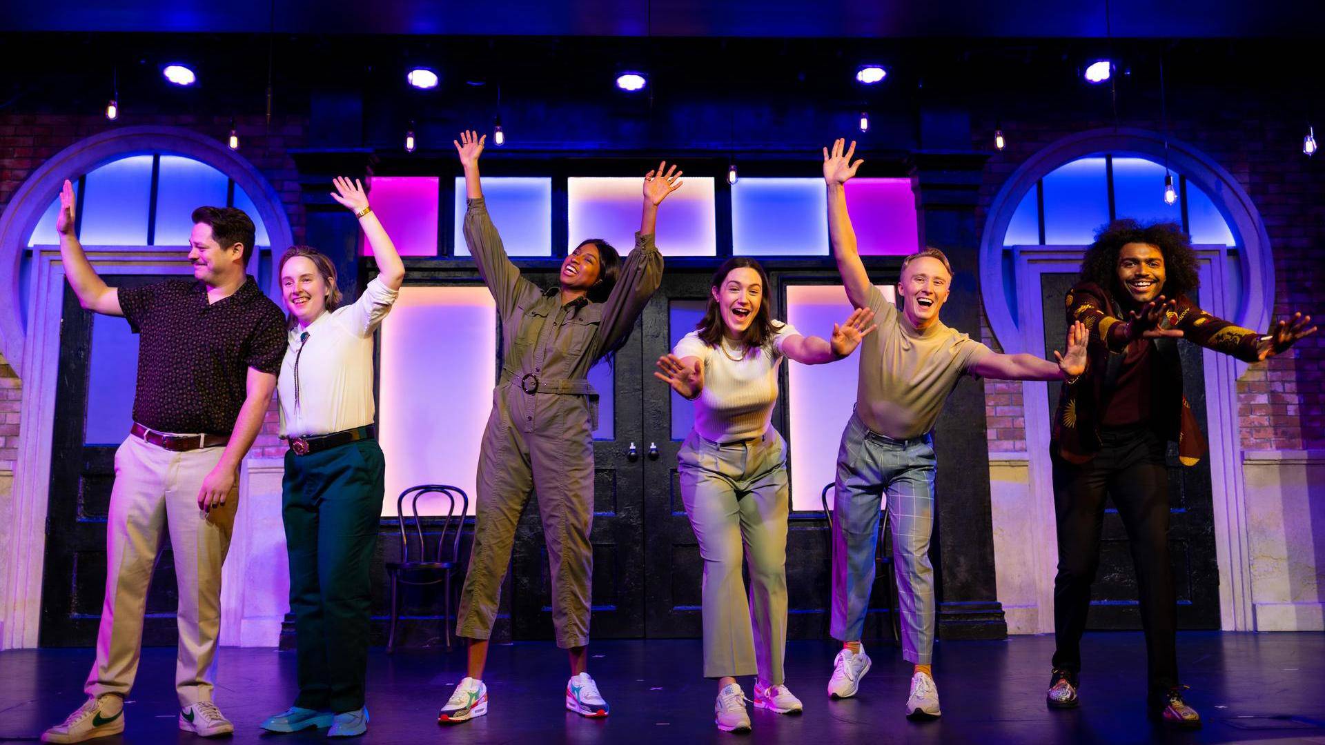 Six diverse young people standing on stage with their hands raised and smiling.