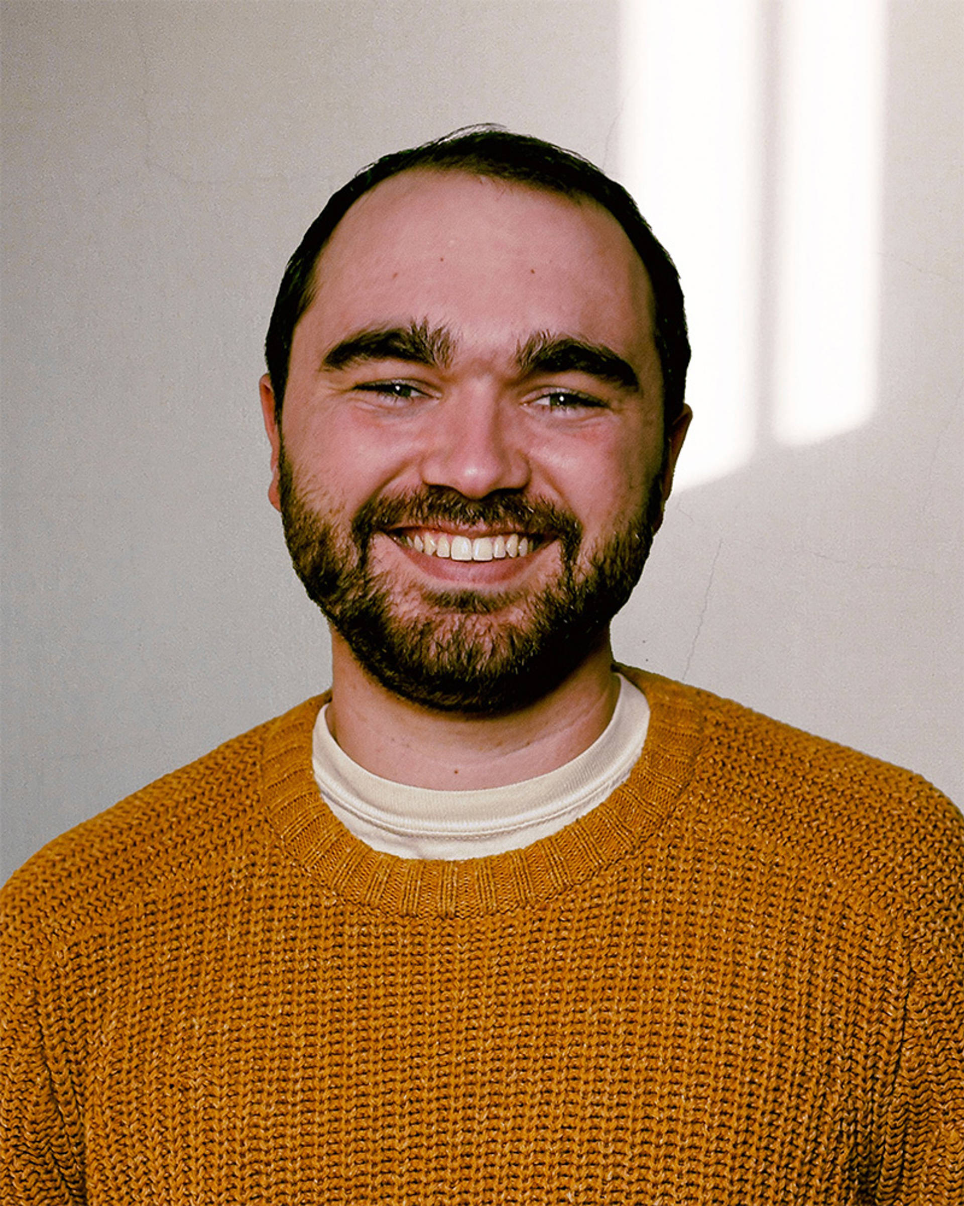 Headshot of a man with light complexion, short dark hair, brown eyes and a gold sweater.
