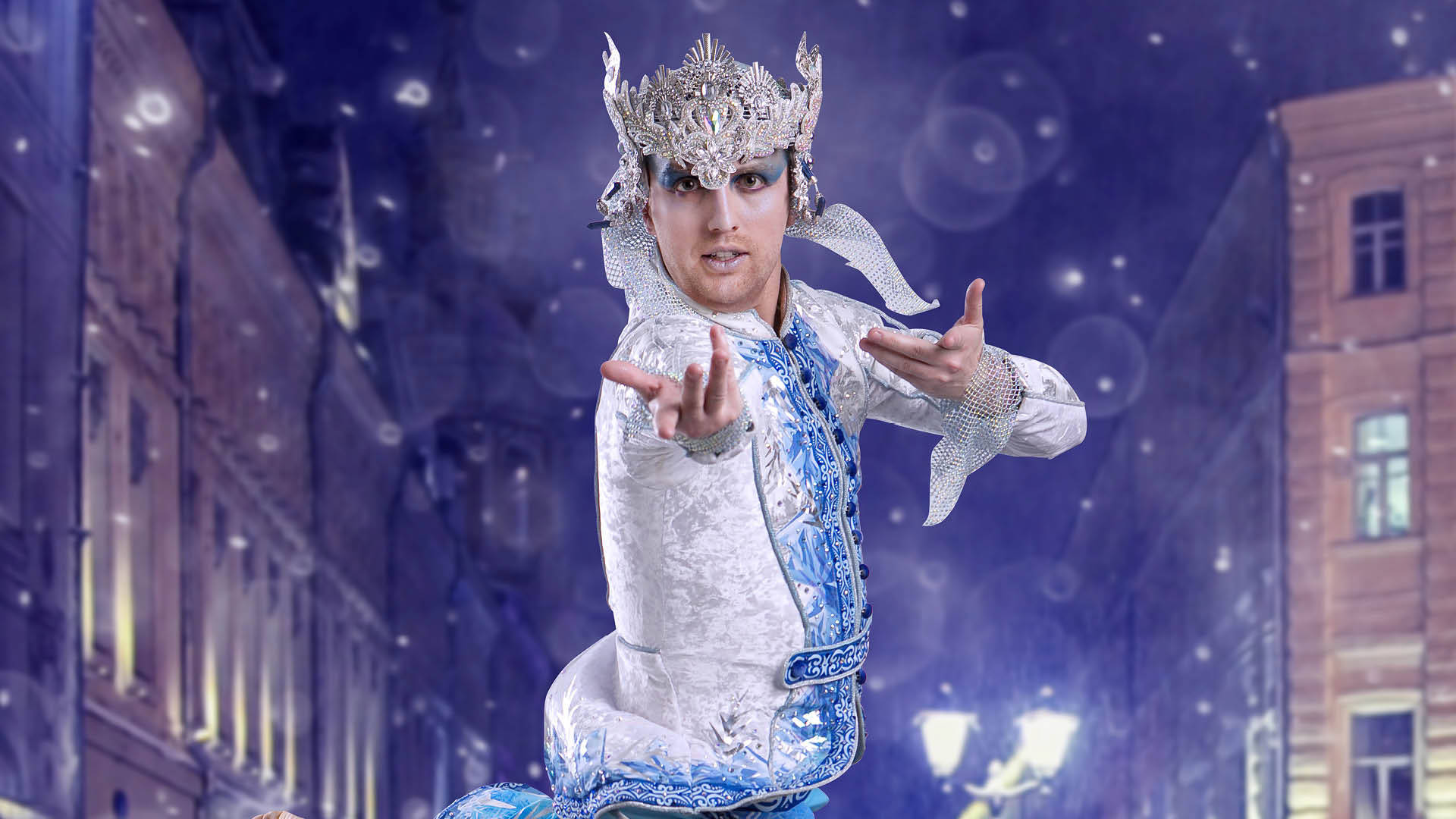 A caucasian dancer in an ornate winter-ice themed white & blue costume and headpiece poses in a snowy night street scene.