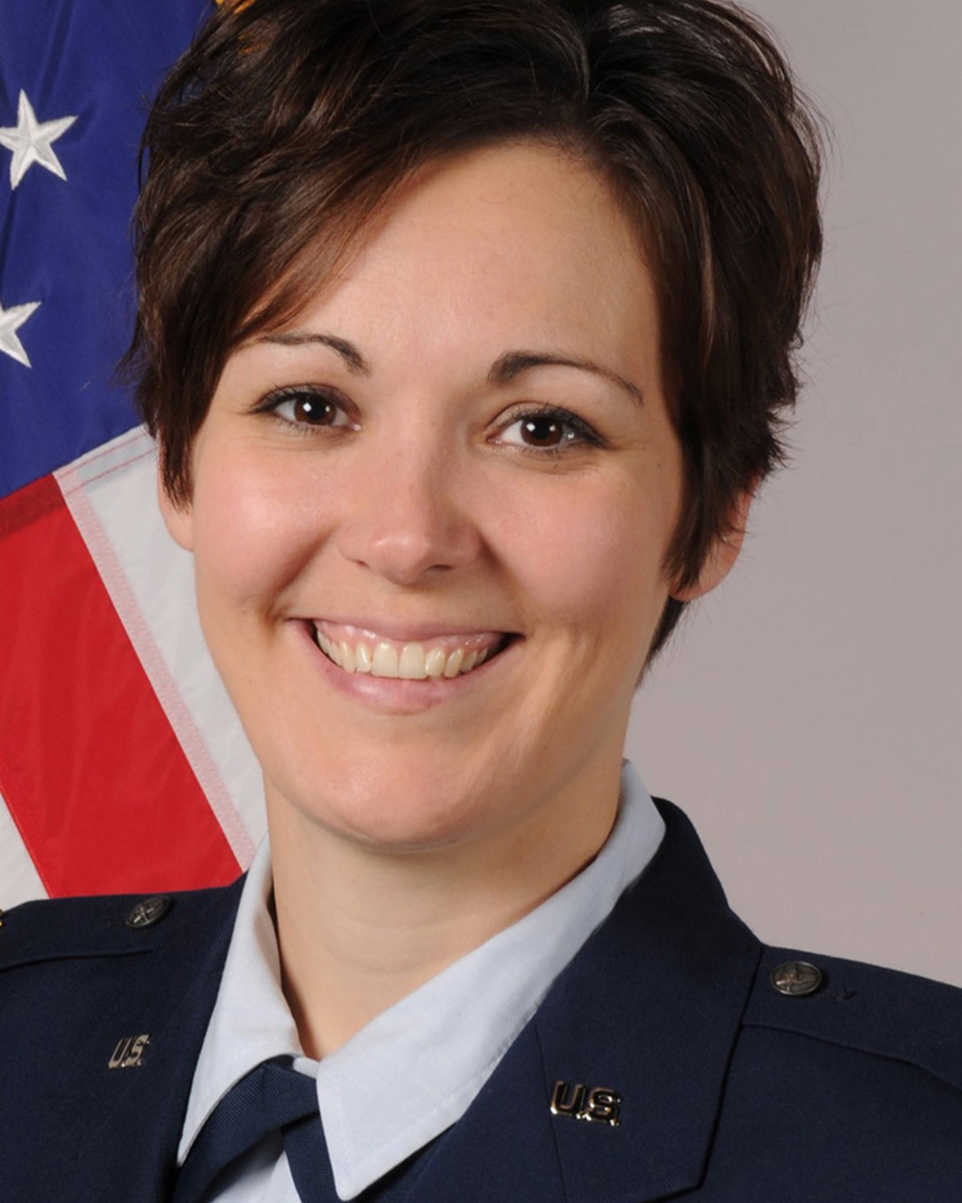 Headhot of a woman with light complexion, brown eyes and medium length hair. She has a navy military outfit on.